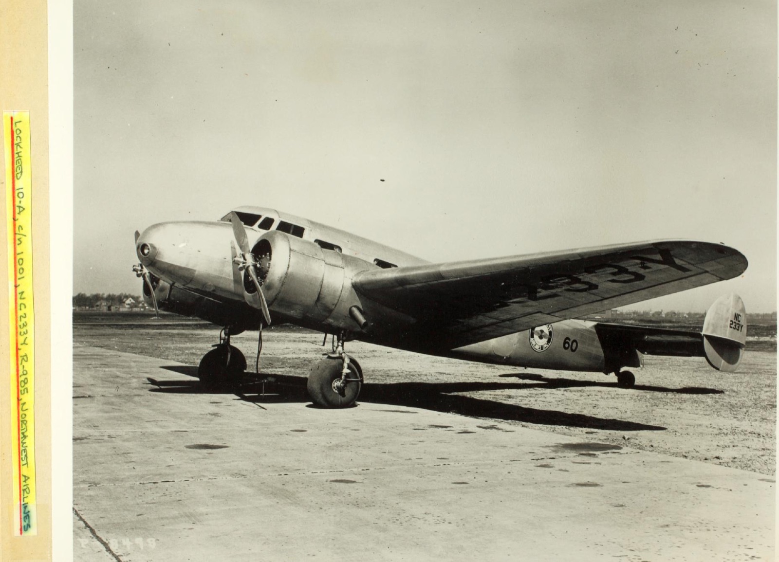 A 1930s archival photograph of a Lockheed Model 10 Electra parked on an airfield — a polished silver twin-engined, twin-tailed monoplane with a rounded nose, seen from the side.