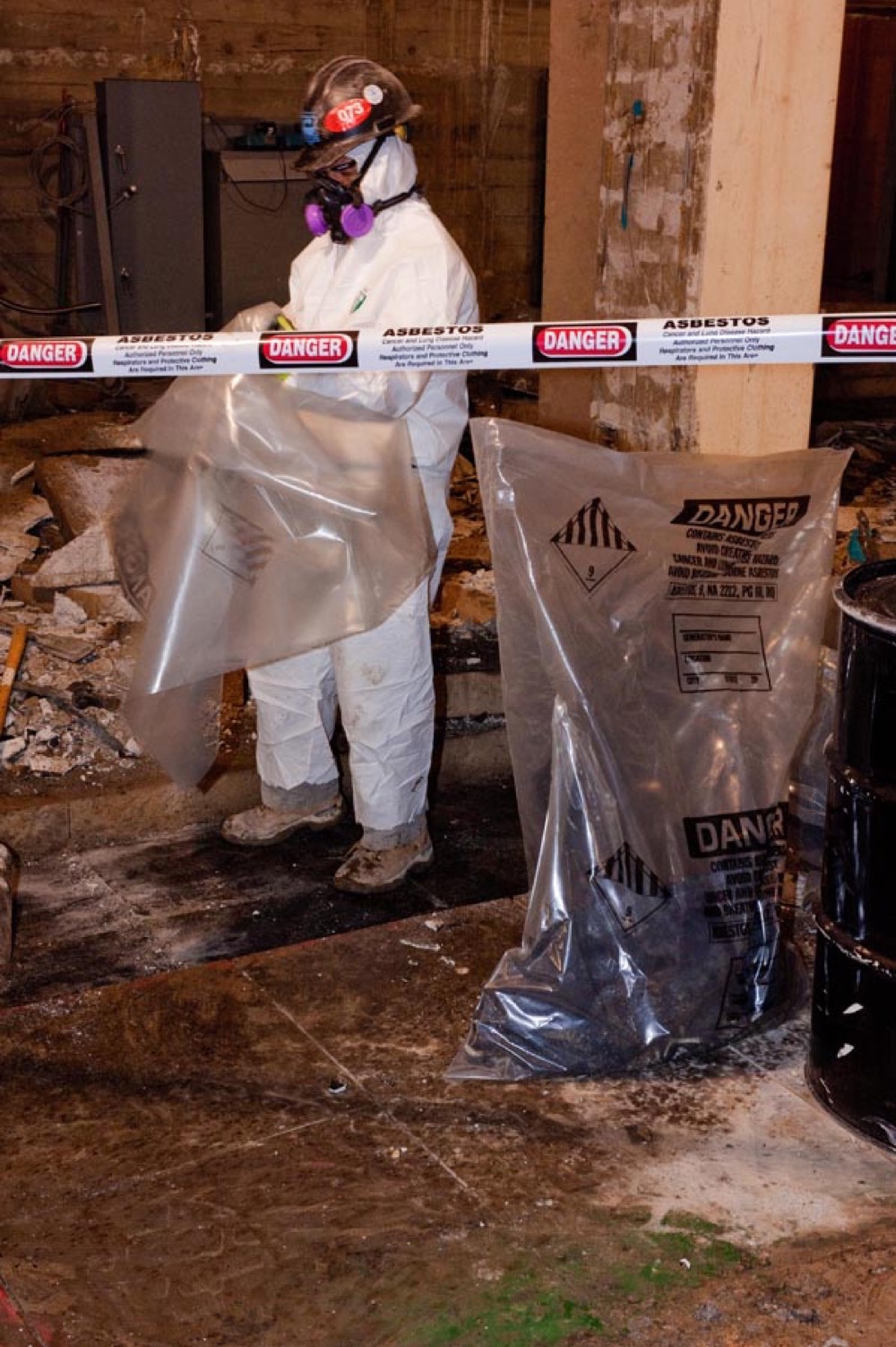 A worker in protective coveralls and respirator performing asbestos abatement, removing asbestos material safely.