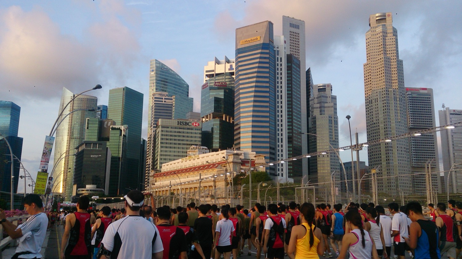 The Singapore financial district skyline, a cluster of modern glass office towers reflected in the water of Marina Bay under a blue sky.