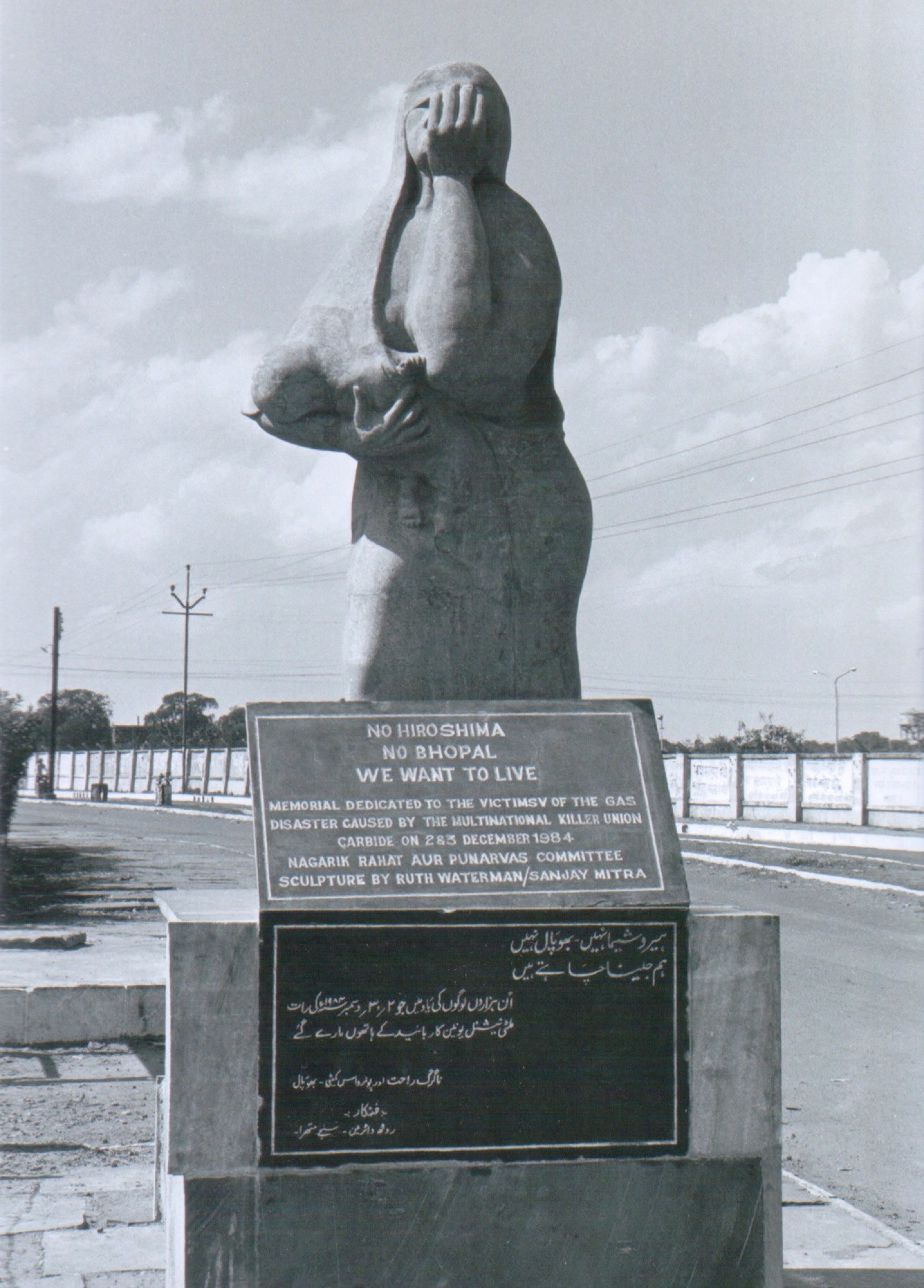The Bhopal disaster memorial statue, a bronze sculpture of a woman shielding a child, photographed in daylight.