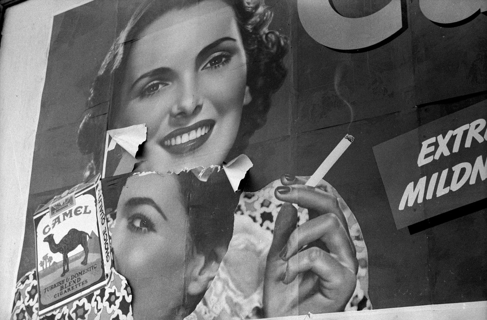 A vintage cigarette advertisement painted on the wall of a small-town building in Woodbine, Iowa, photographed in 1940. The faded paint shows a cigarette-pack logo and slogan.