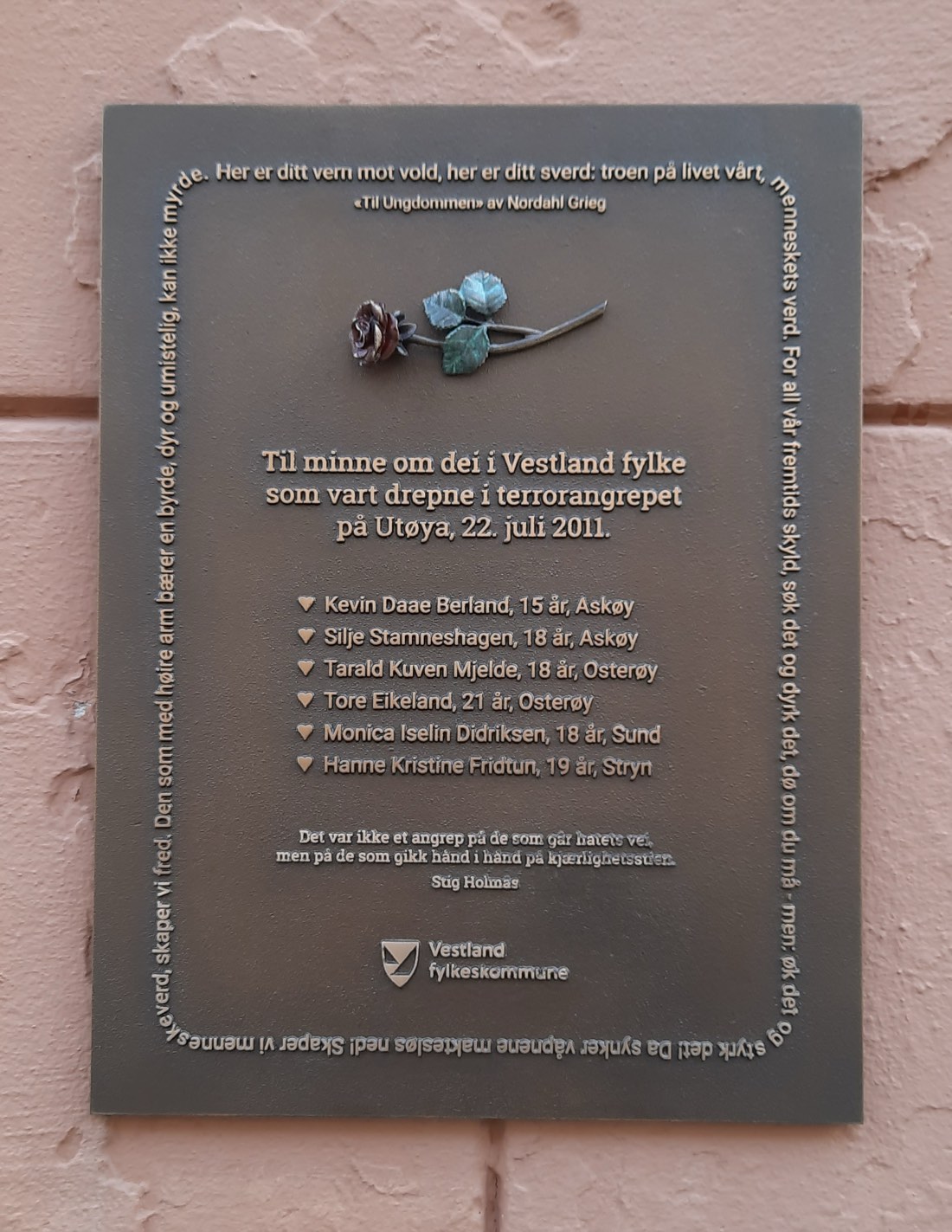 A memorial plaque in Bergen, Norway, commemorating the victims of the 22 July 2011 Utøya attack, set against a stone wall.