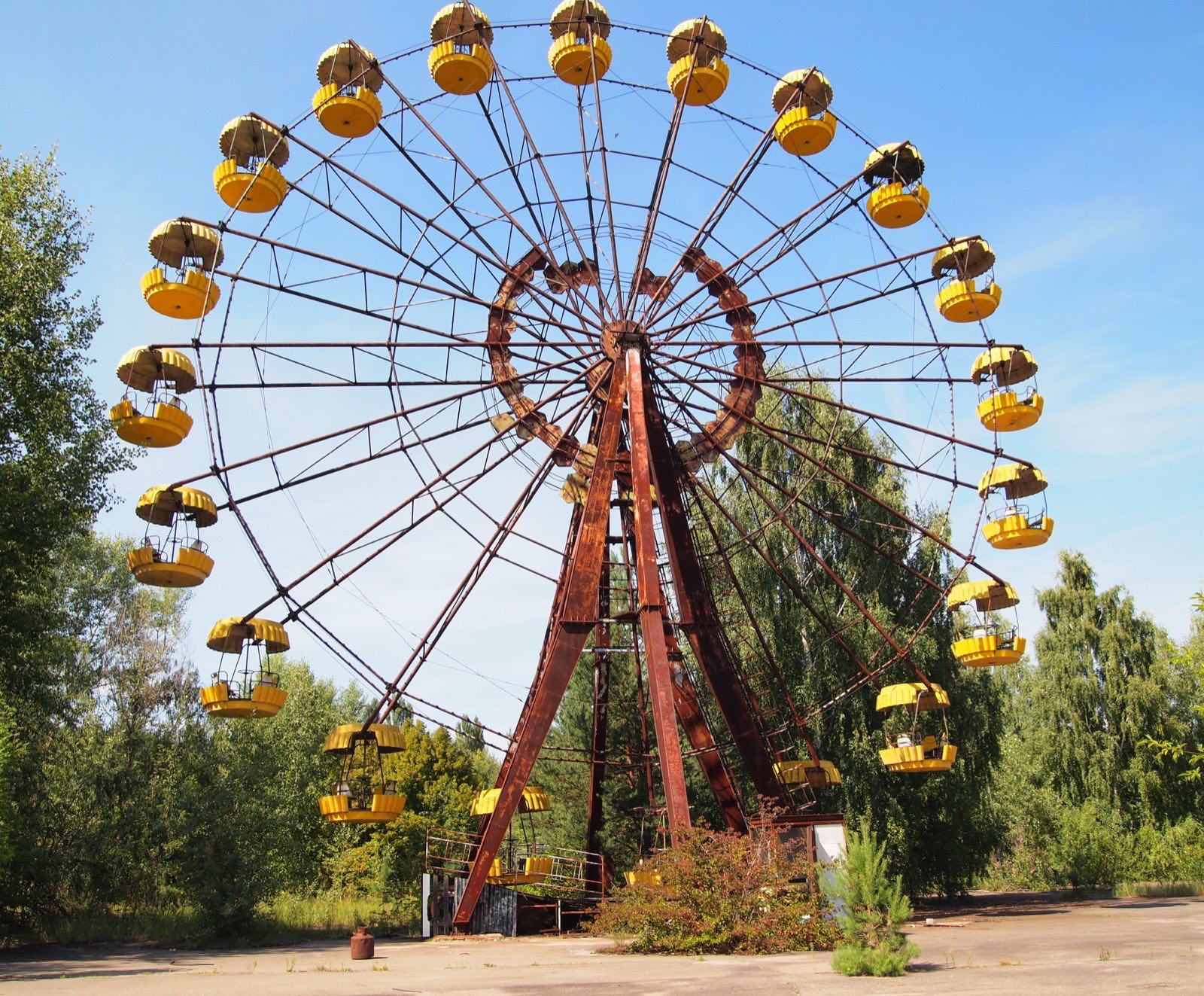 The abandoned ferris wheel in Pripyat amusement park, photographed in daylight against a cloudy sky. The yellow cabin compartments are rusted.