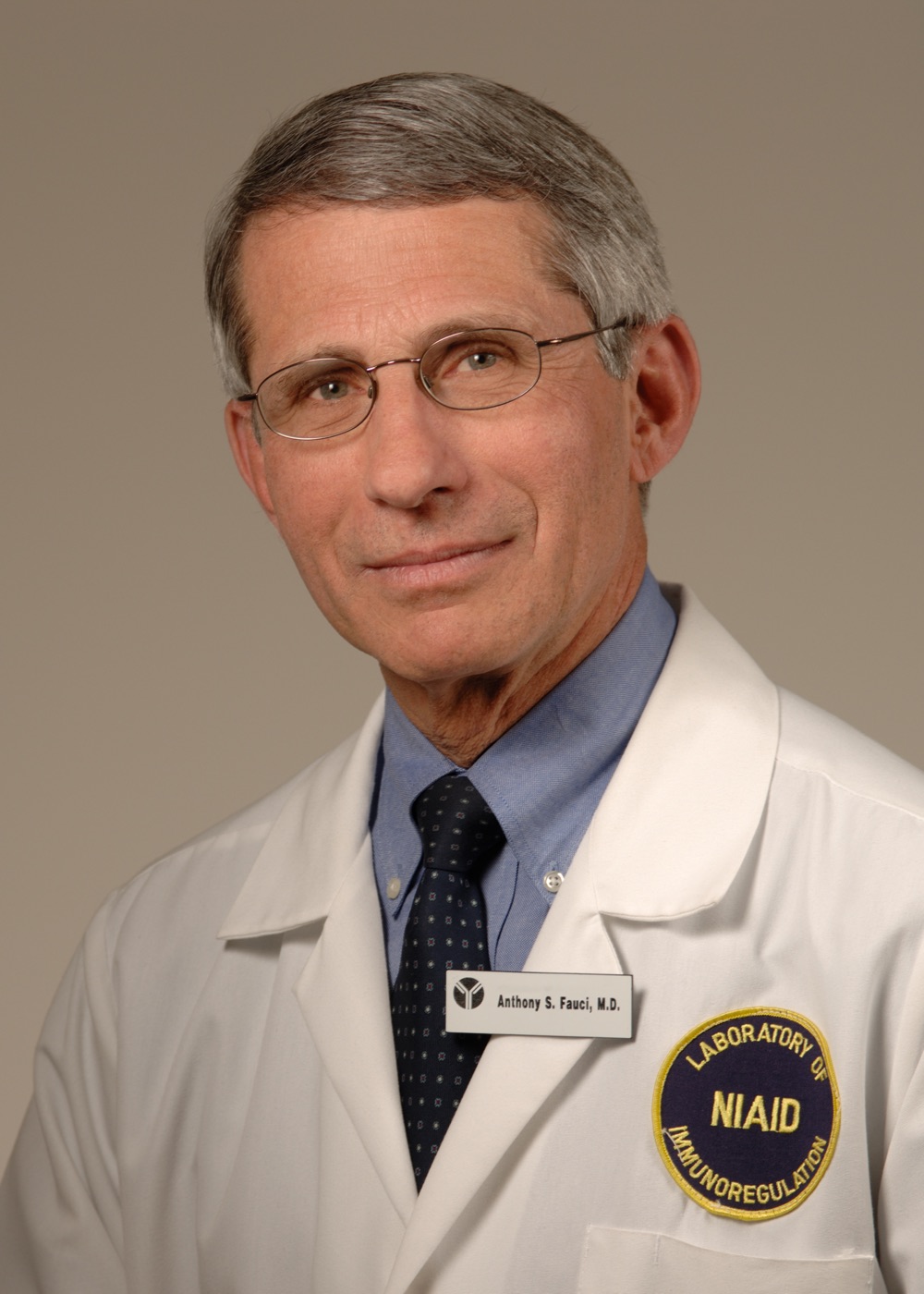 Anthony S. Fauci, M.D., in his official NIAID Director portrait — middle-aged man with grey hair, wearing dark suit, light shirt, and patterned tie, photographed against a soft neutral background.