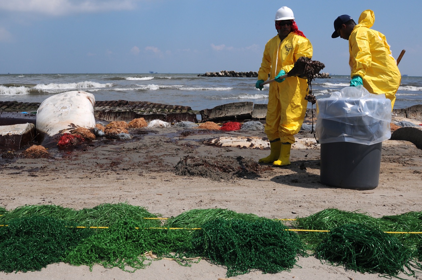 Workers in protective gear cleaning up oil on Port Fourchon beach in Louisiana during the Deepwater Horizon spill.