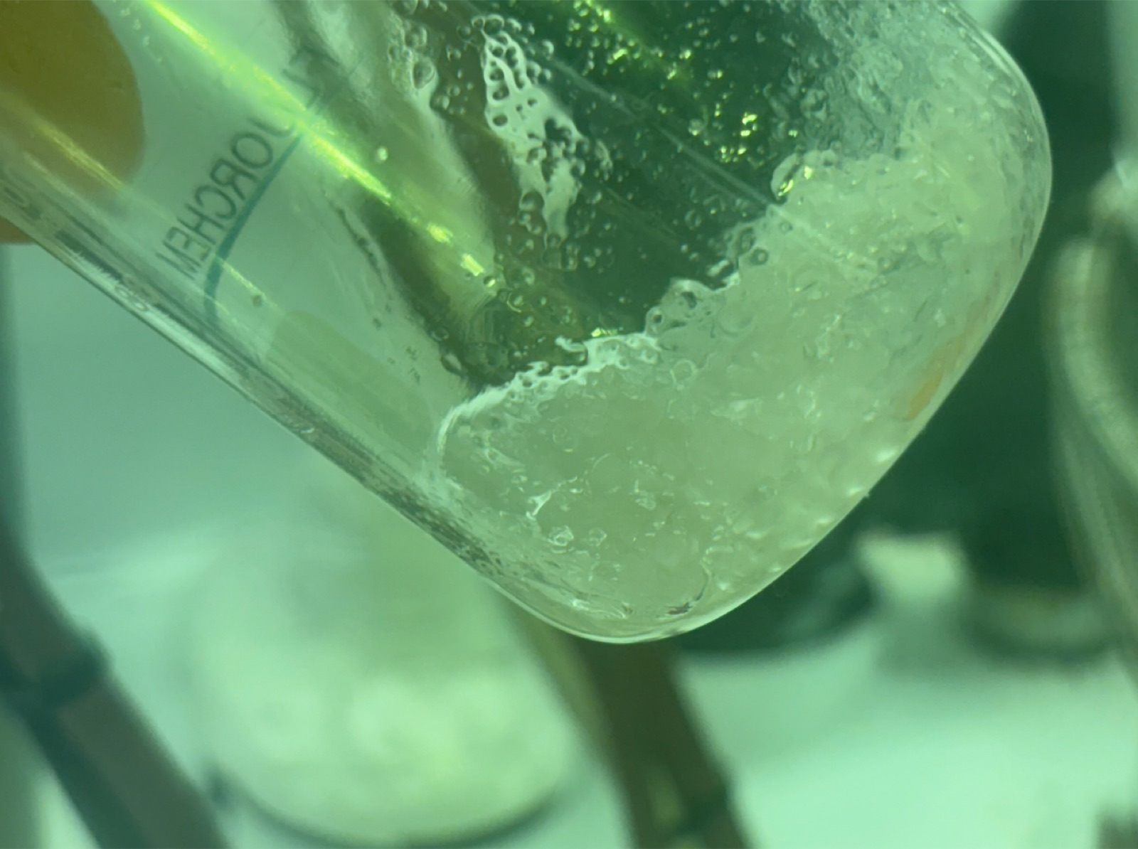 A small beaker containing PFOA chemical (perfluorooctanoic acid) — a white-yellow waxy solid, photographed on a laboratory bench.