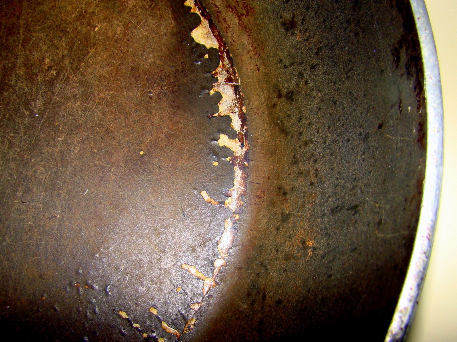 A Teflon-coated non-stick frying pan, photographed on a kitchen surface — the black PTFE coating visible on the cooking surface, a wooden handle, slight wear on the surface from use.