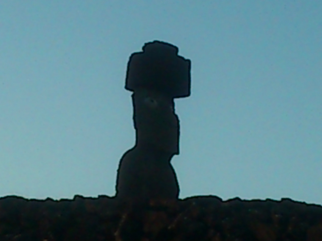 A single restored moai with a red cylindrical topknot and white inlaid eyes, standing against the sky.