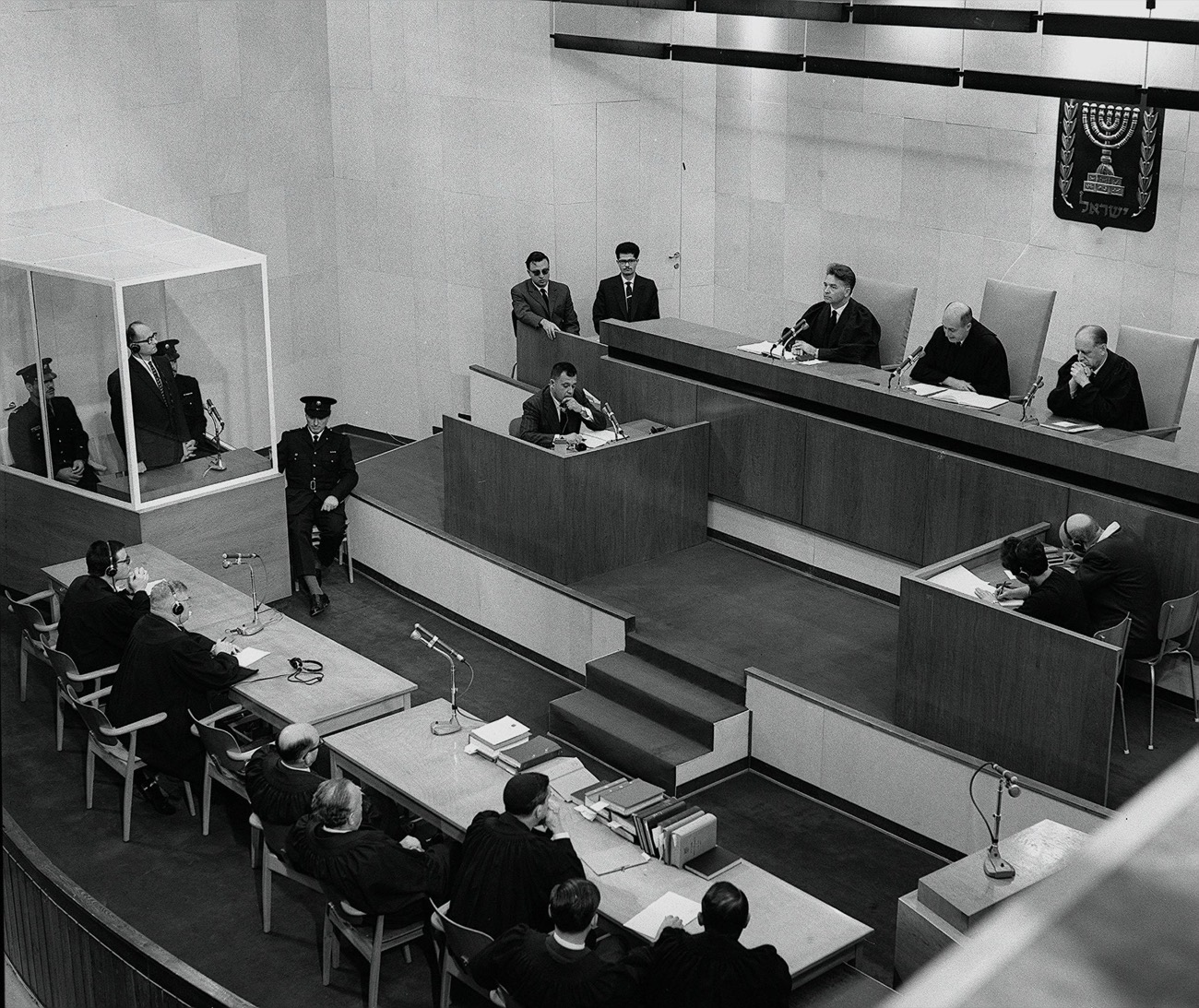 Adolf Eichmann standing in the glass booth as the court delivers its judgement at the conclusion of his trial.
