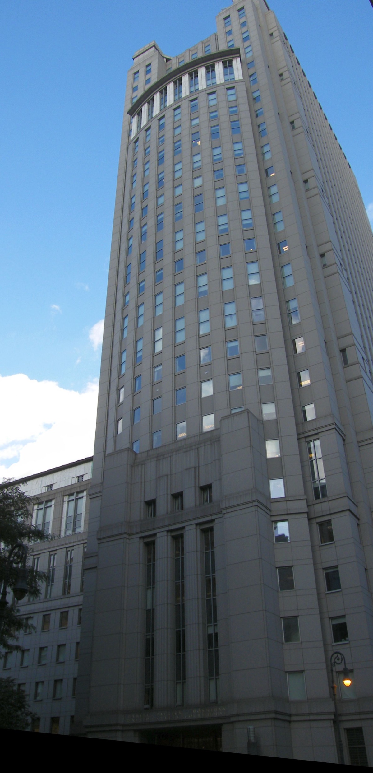The Daniel Patrick Moynihan U.S. Courthouse in lower Manhattan — a tall classical limestone tower with Corinthian columns and a stepped pyramid roof, photographed from street level looking up.
