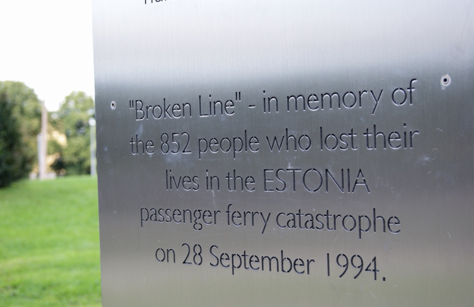 The Broken Line memorial in Tallinn — a curving structure of metal that appears severed in the middle, symbolising a journey cut short, set on a stone plaza.