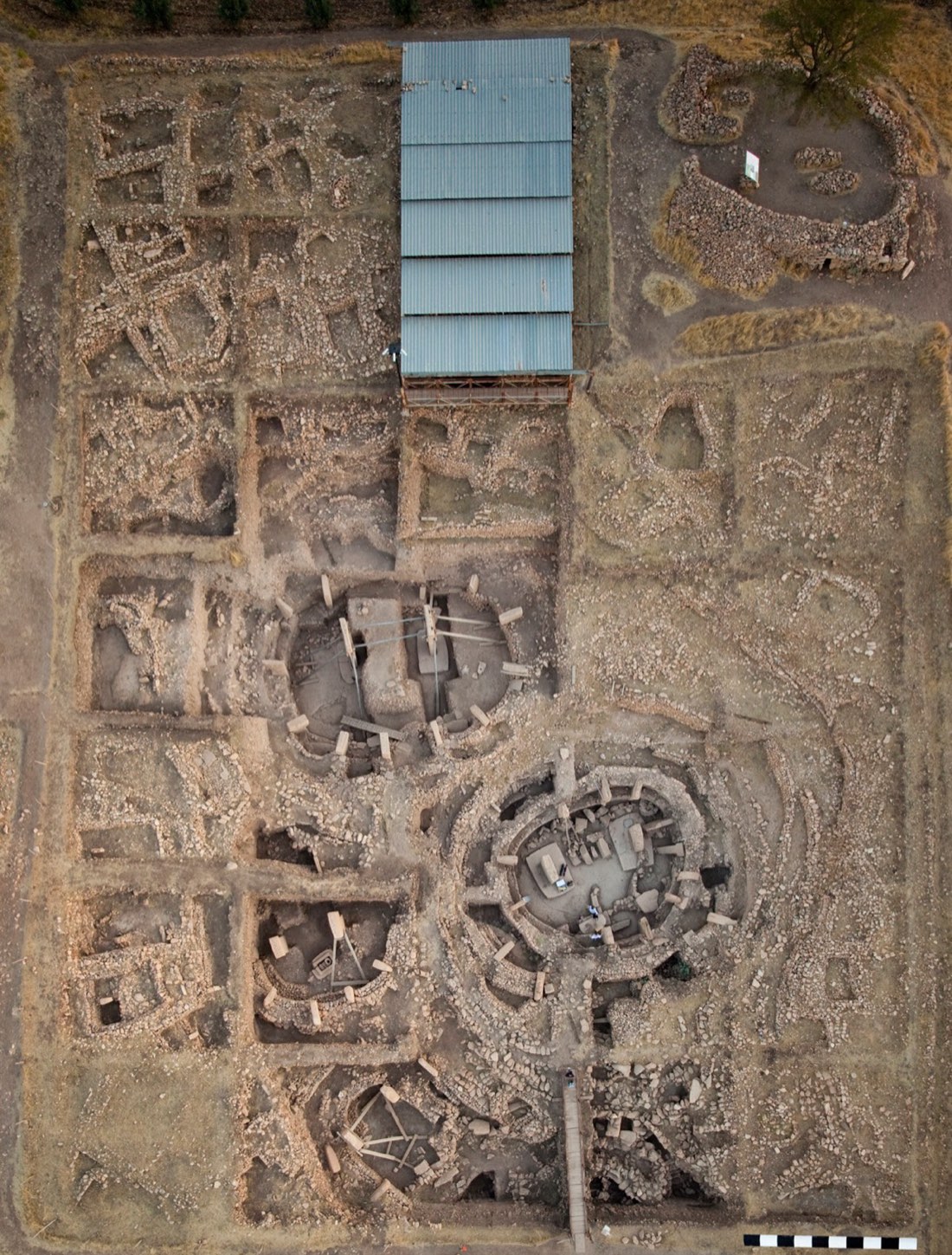 An overhead view of the main excavation area of Göbekli Tepe, showing several circular enclosures of stone pillars under a protective roof.
