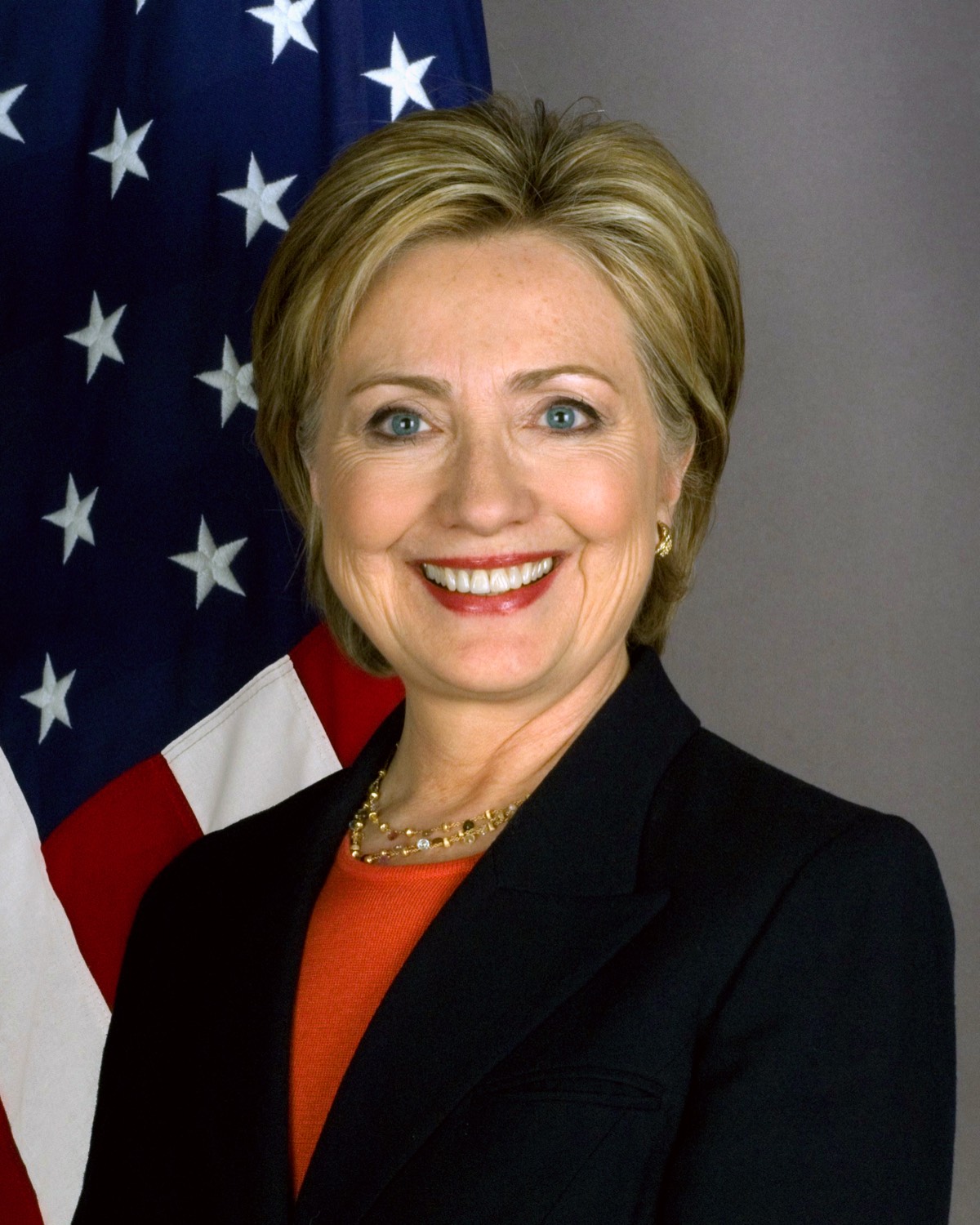 The official United States Secretary of State portrait of Hillary Clinton, seated in front of an American flag.