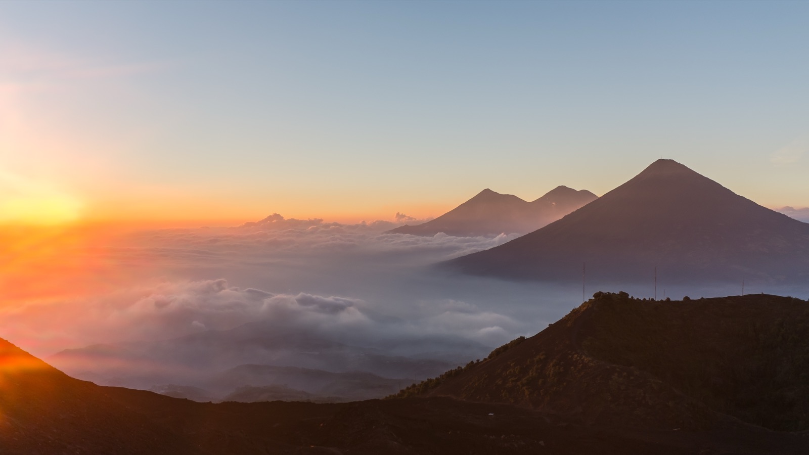 A wide view of the Guatemalan landscape seen from Volcano Pacaya: green volcanic hills and valleys stretching to distant mountains under a cloudy sky.