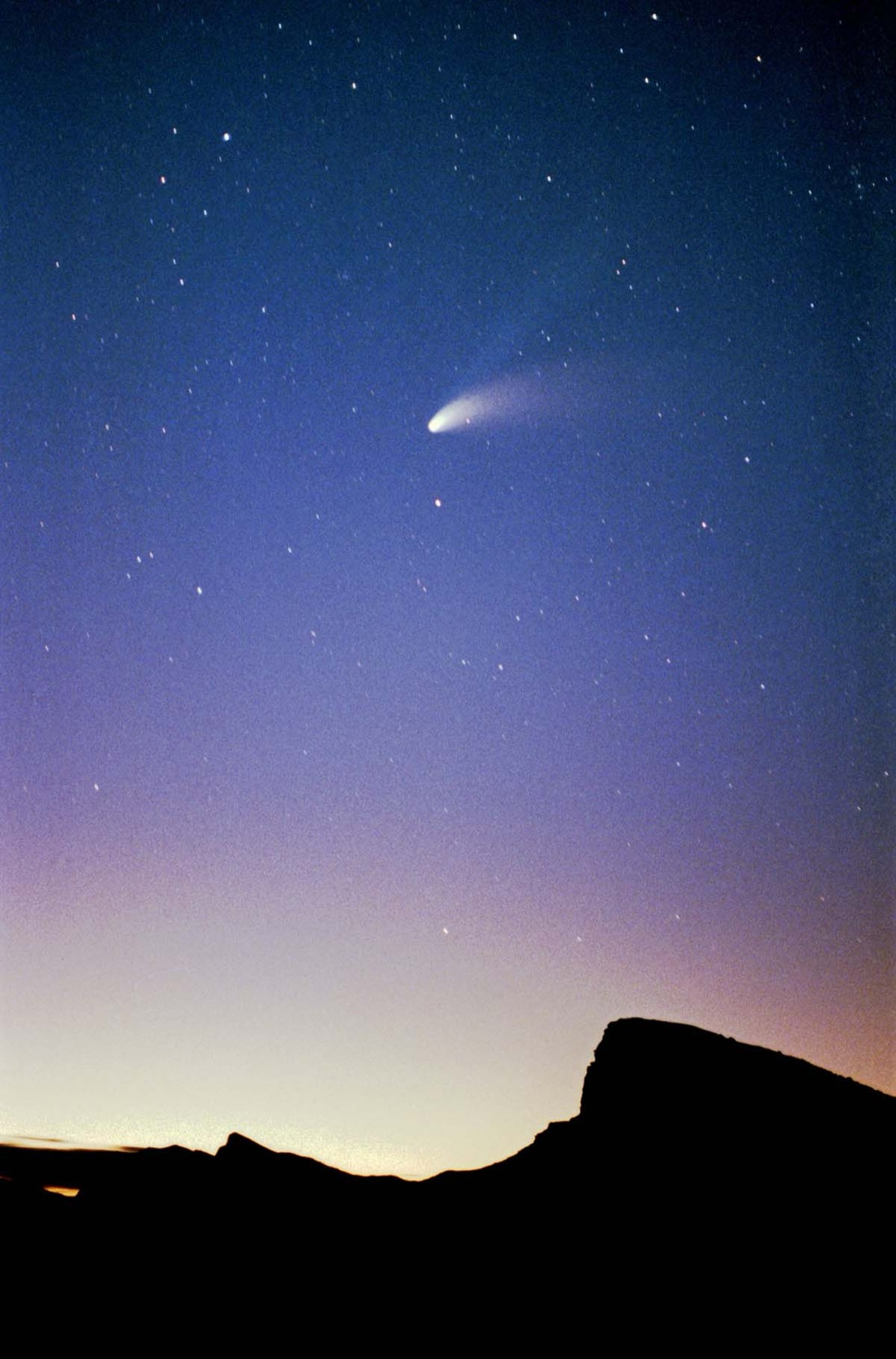 The comet Hale-Bopp shining in the night sky over Death Valley in 1997, with its bright tail visible above a dark landscape.