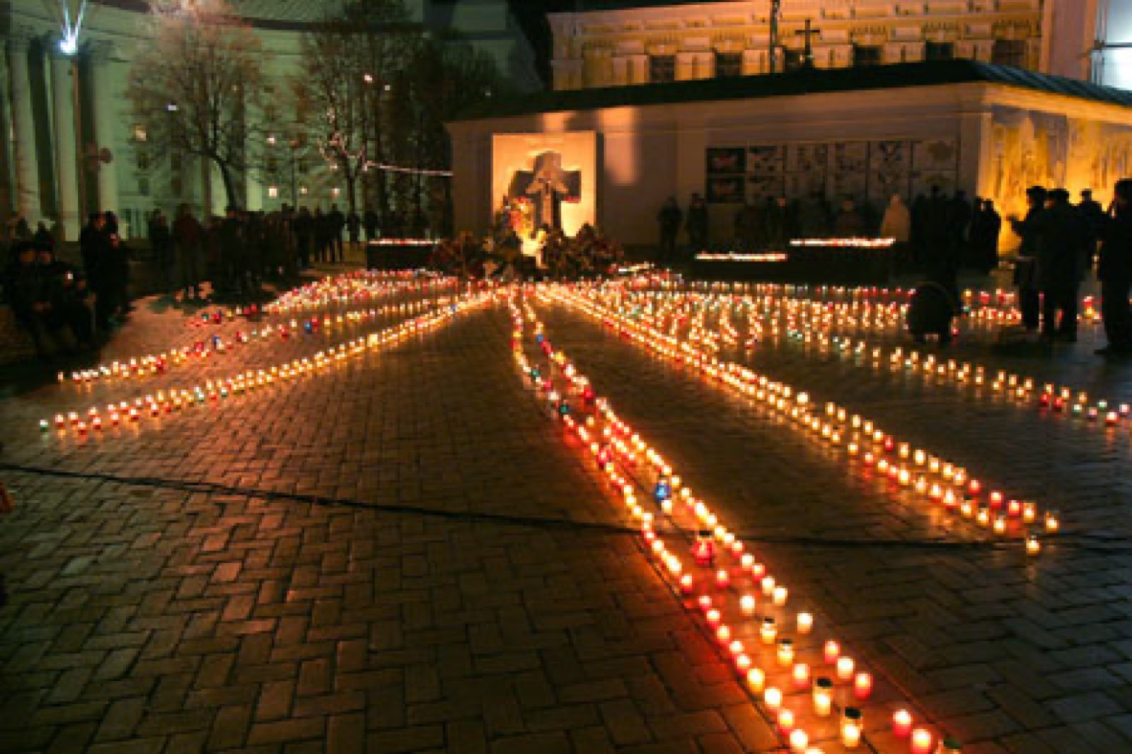 Lit memorial candles arranged in rows on a Kyiv pavement at night during a Holodomor commemoration — small flickering flames against dark stone.
