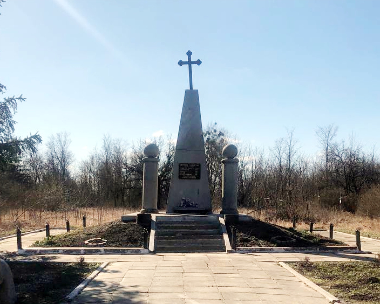 The Holodomor memorial monument in Kyiv — a bronze figure of an emaciated child holding wheat against a stone wall, set in a contemplative public garden.