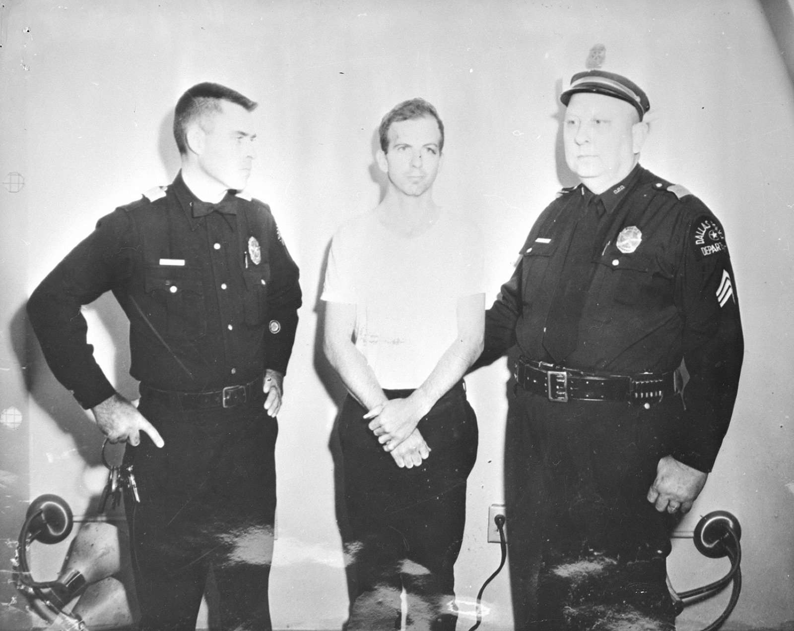 Lee Harvey Oswald in a mug shot photograph — 24 years old, dark hair, wearing a dark shirt.