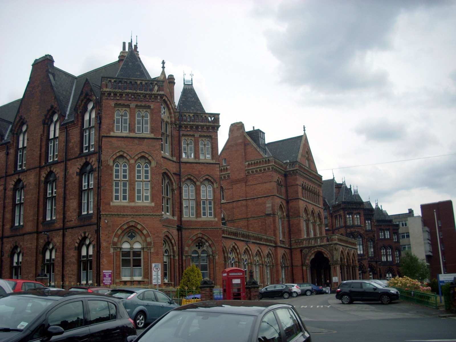 Leeds General Infirmary viewed from Great George Street — a large Victorian Gothic Revival hospital building with red brick walls, stone window dressings, and a tall central clock tower.