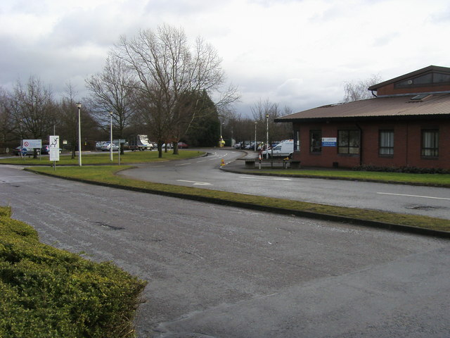 The main entrance to Stoke Mandeville Hospital in Aylesbury, Buckinghamshire, with the ambulance station alongside — modern brick and glass buildings with directional signage.