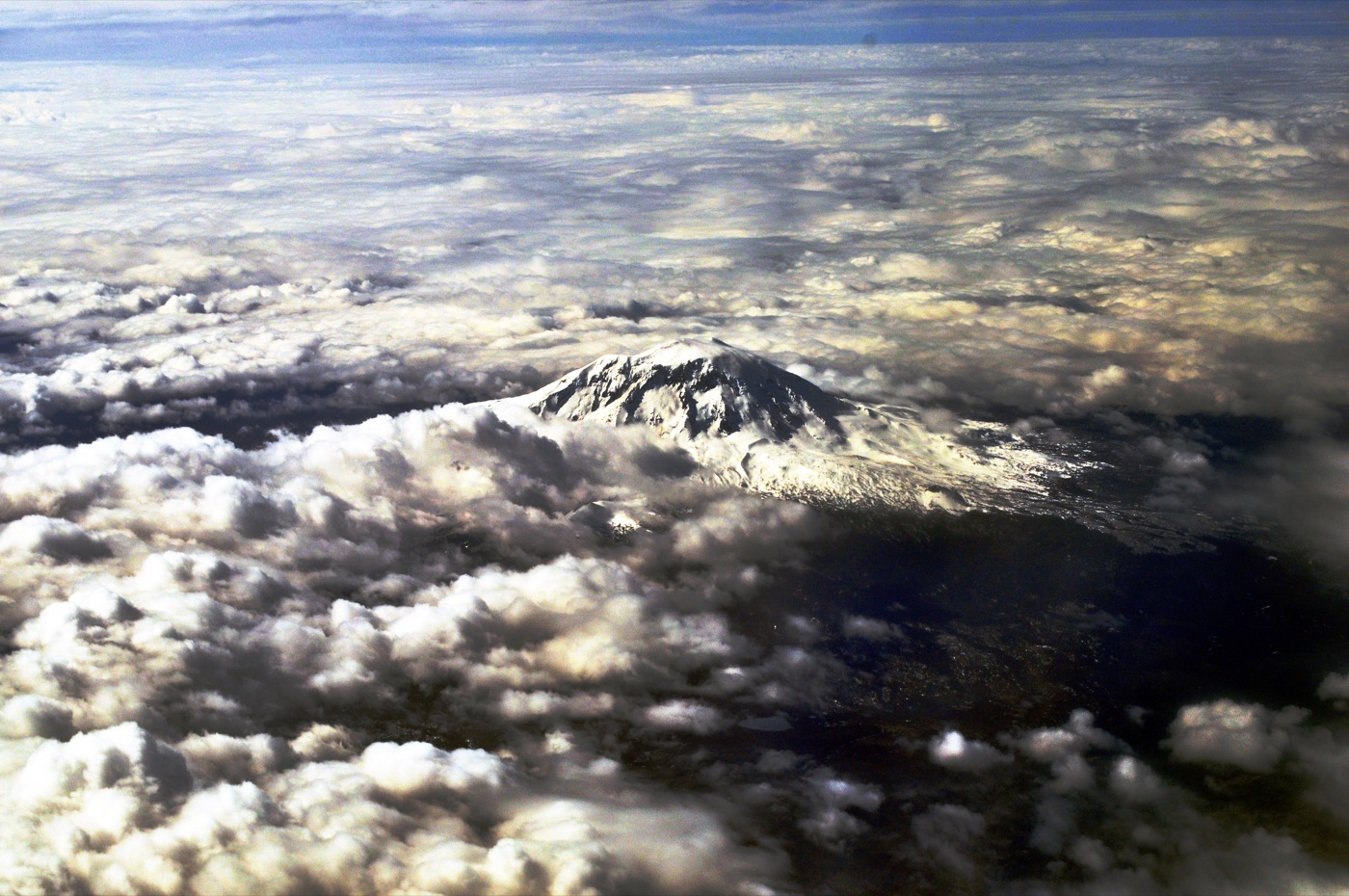 An aerial view of the snow-capped Mount Rainier in Washington state, rising above the clouds.