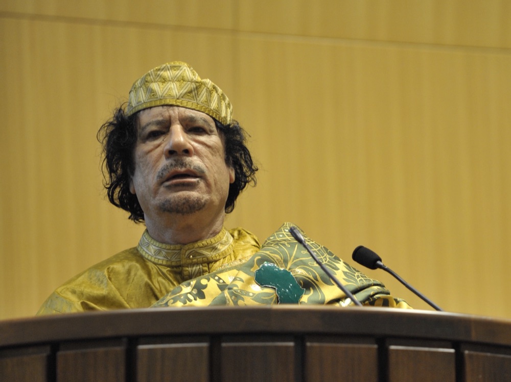 Muammar al-Gaddafi at the African Union Summit, February 2009 — older man with grey beard wearing traditional Libyan robe and headwear, photographed from chest up in a public appearance.