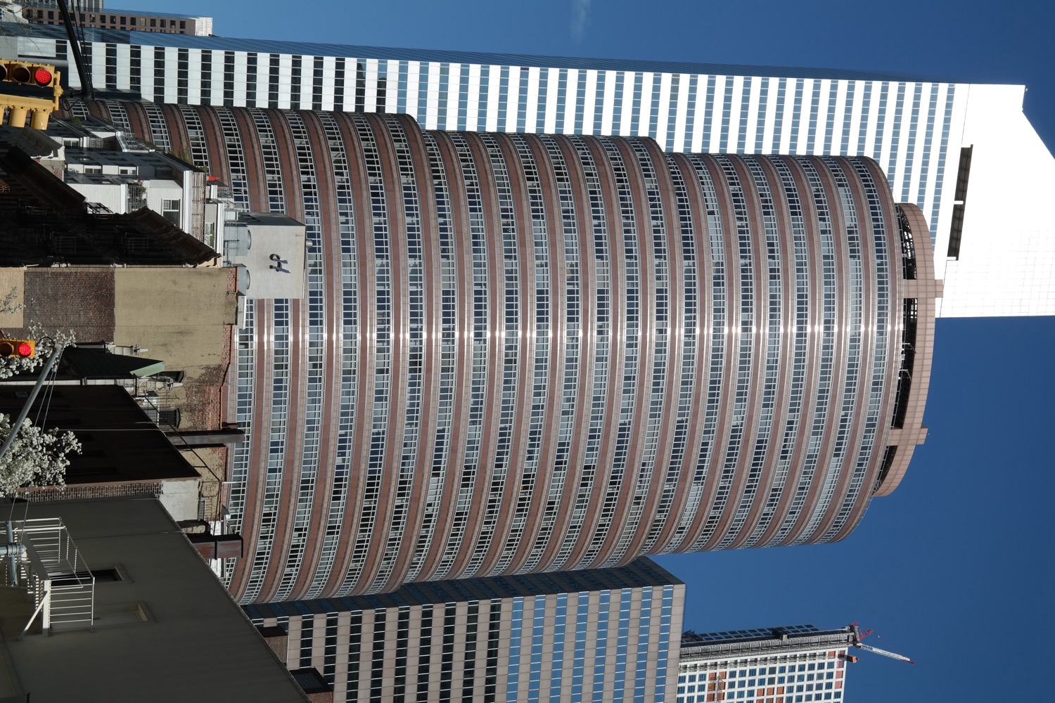 The Lipstick Building in Midtown Manhattan, a distinctive oval-shaped red-and-pink granite skyscraper that tapers in tiers like a tube of lipstick, against a blue sky.