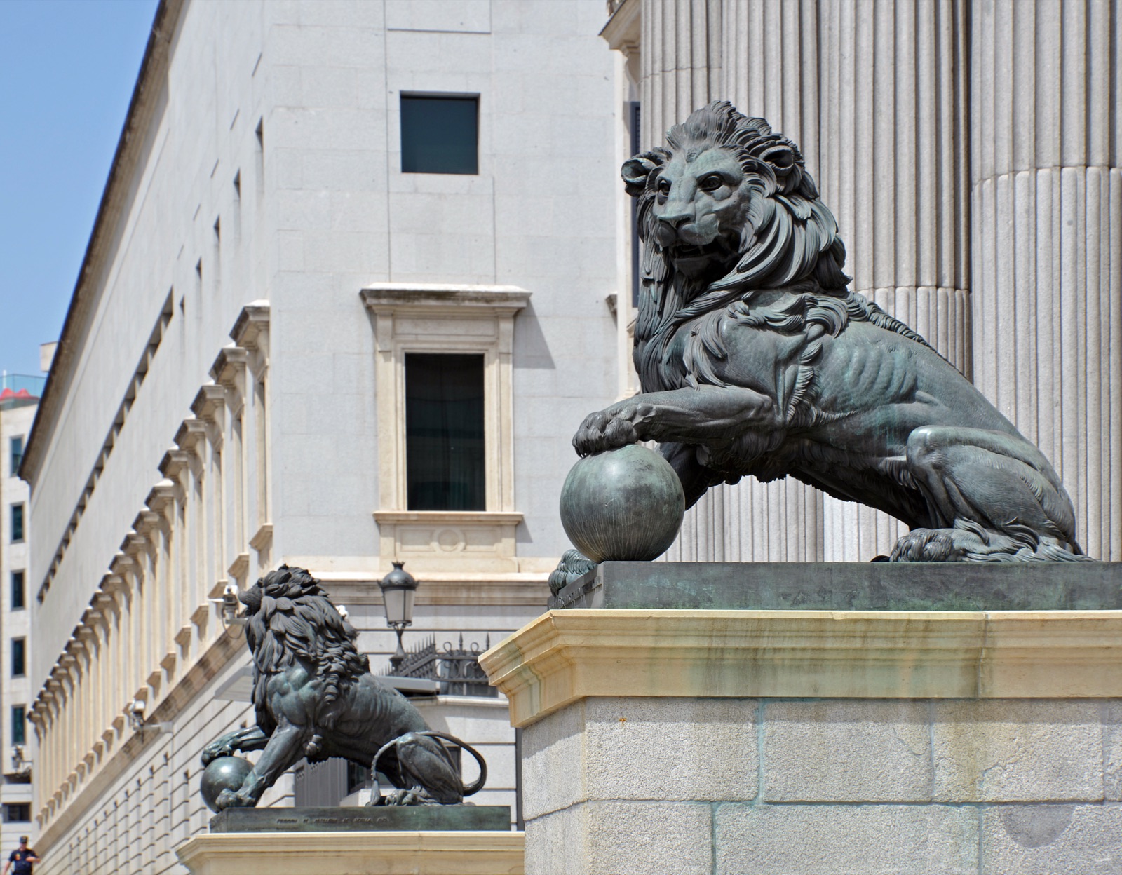 The neoclassical facade of the Congreso de los Diputados, the lower house of the Spanish parliament in Madrid — a columned portico approached by steps flanked by two large bronze lions, beneath a triangular pediment.