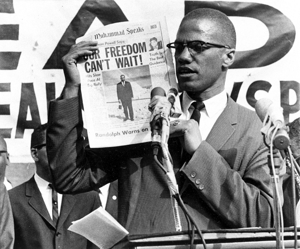 Malcolm X in 1963 holding a copy of the Nation of Islam newspaper Muhammad Speaks.