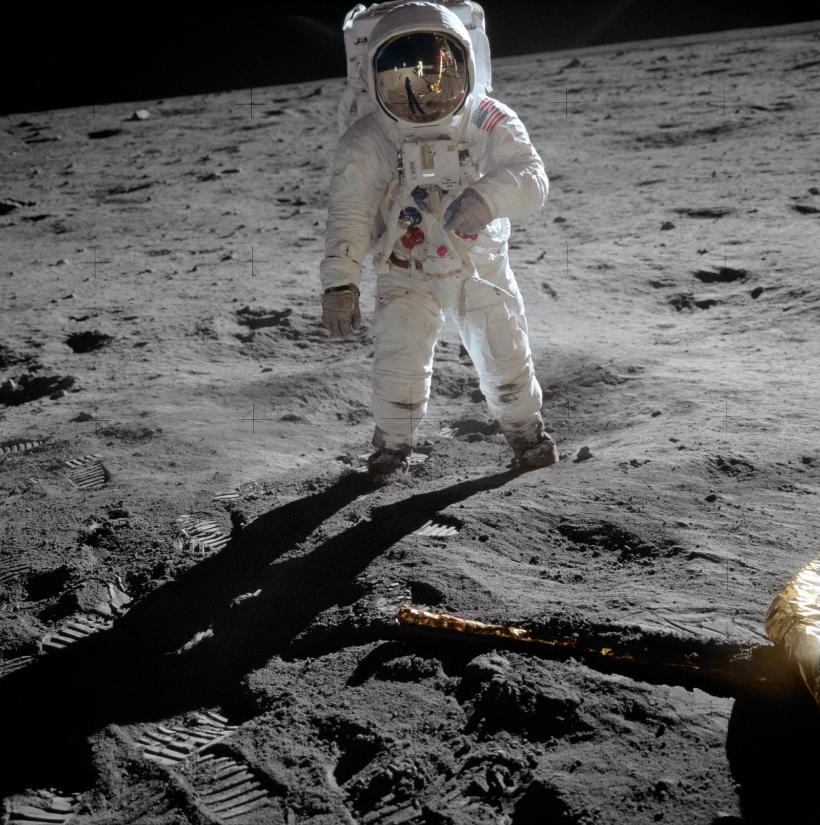Buzz Aldrin standing on the lunar surface during Apollo 11, photographed by Neil Armstrong. The Lunar Module, scientific equipment, and Armstrong himself are reflected in Aldrin's gold visor.
