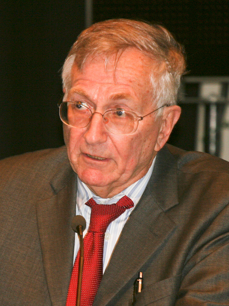 Seymour Hersh in a contemporary photograph — older man with grey hair and beard, wearing a sport coat, photographed in profile against a soft background.