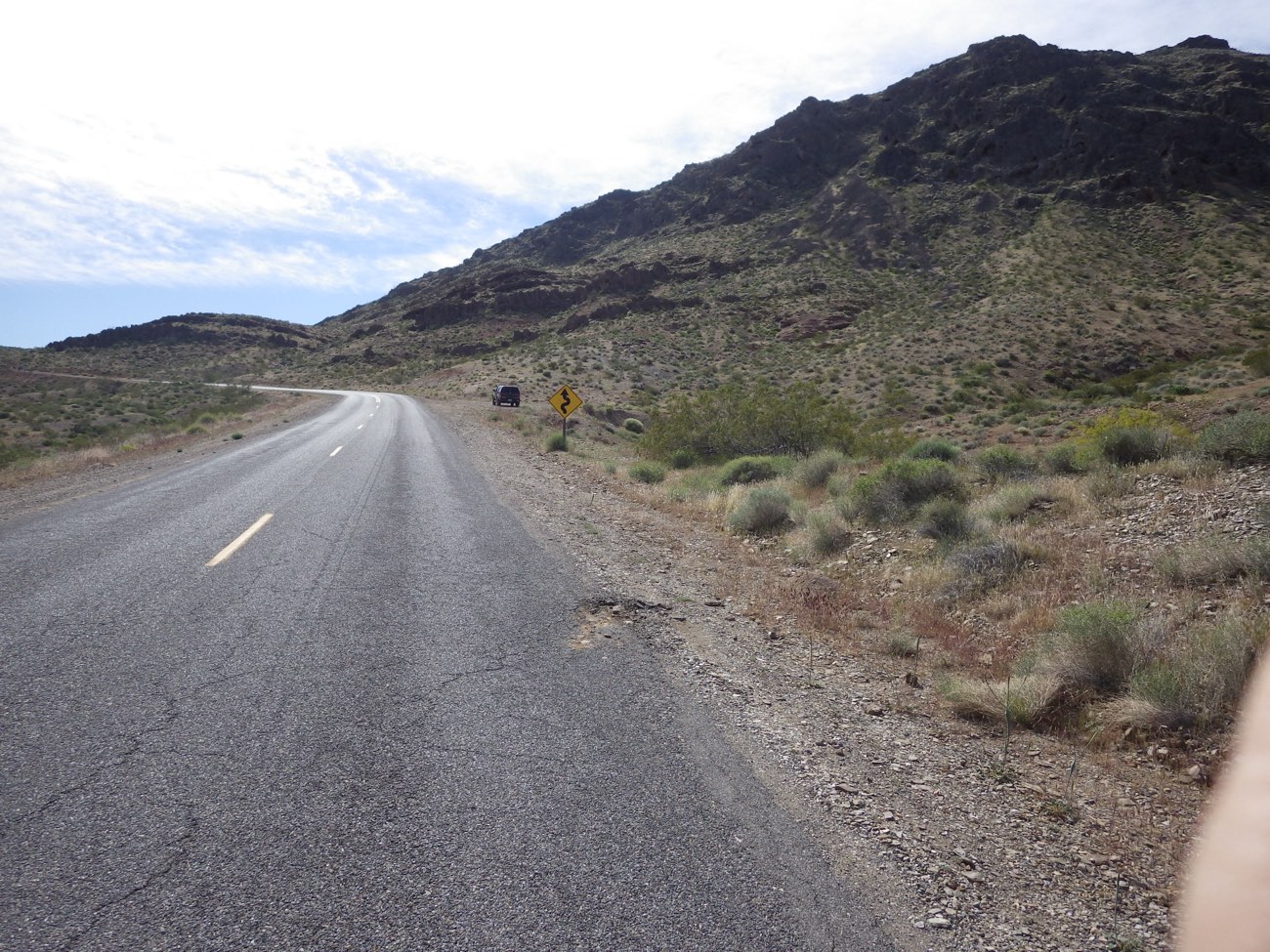 A road cutting through a desert hillside in the American Southwest, sloping down into arid terrain.
