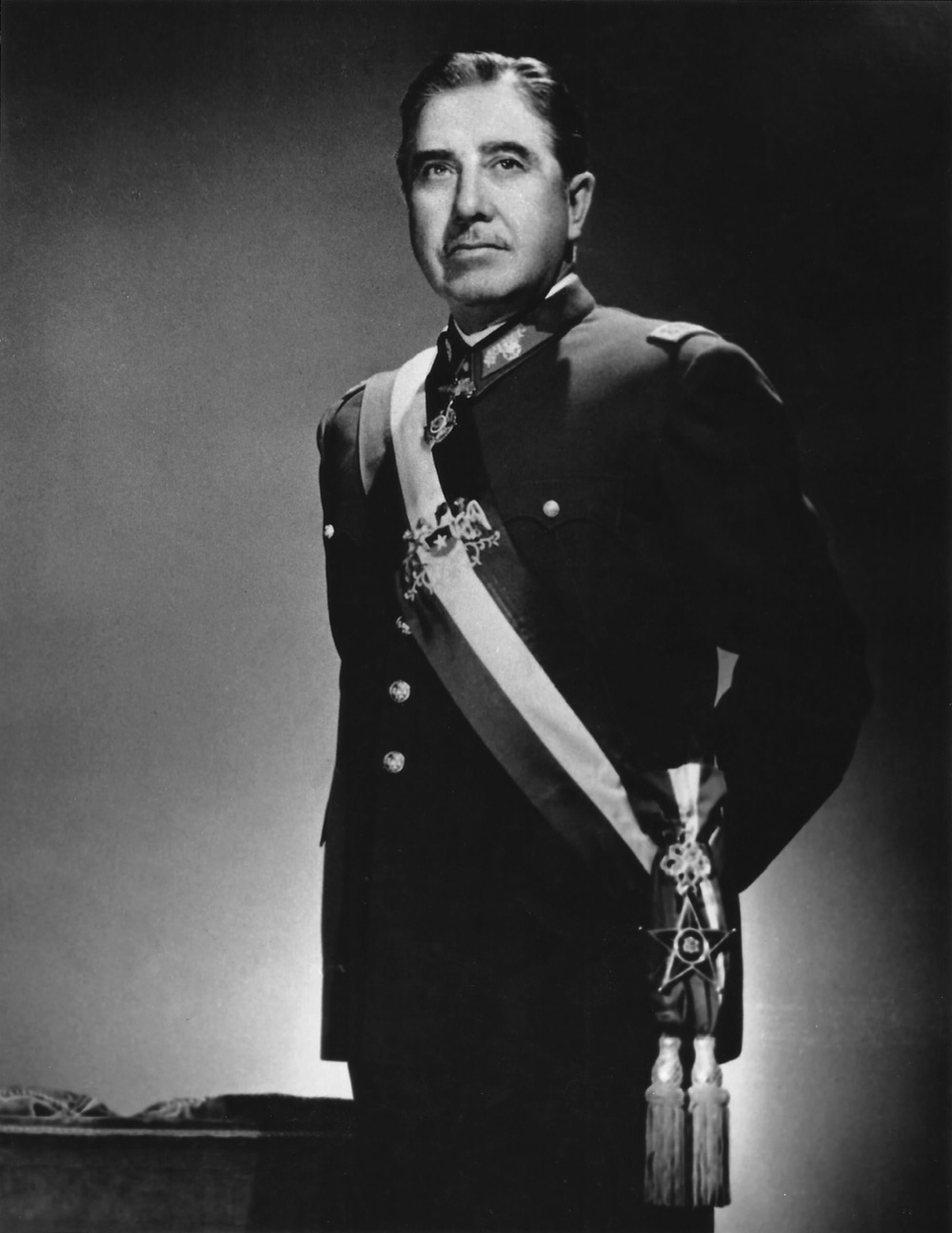 Augusto Pinochet in his official military portrait — the Chilean military dictator in a dark green uniform with general's insignia, peaked cap, formal pose against a neutral background.