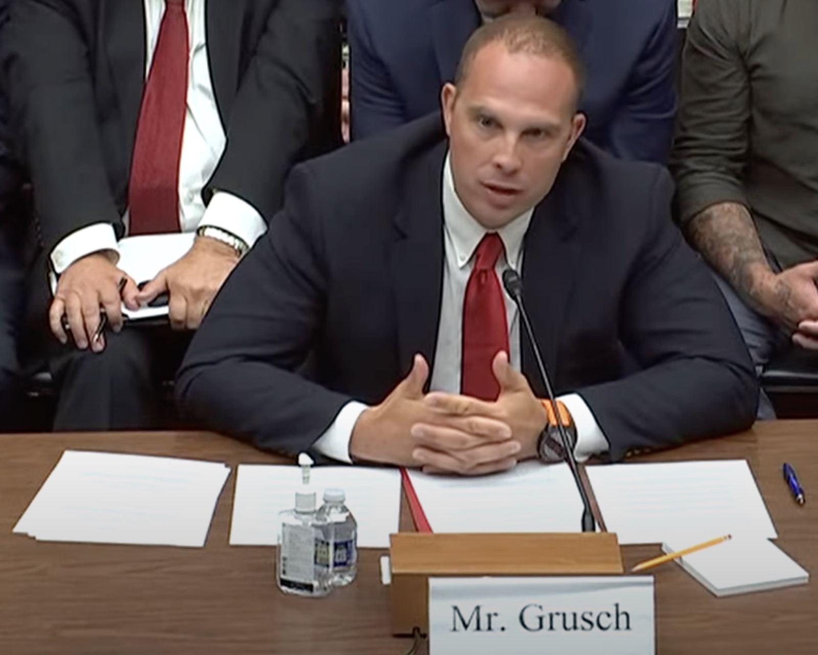 David Grusch giving sworn testimony before the U.S. House Subcommittee on National Security, the Border and Foreign Affairs on July 26, 2023 — dark suit, dark tie, raised right hand, microphone before him.