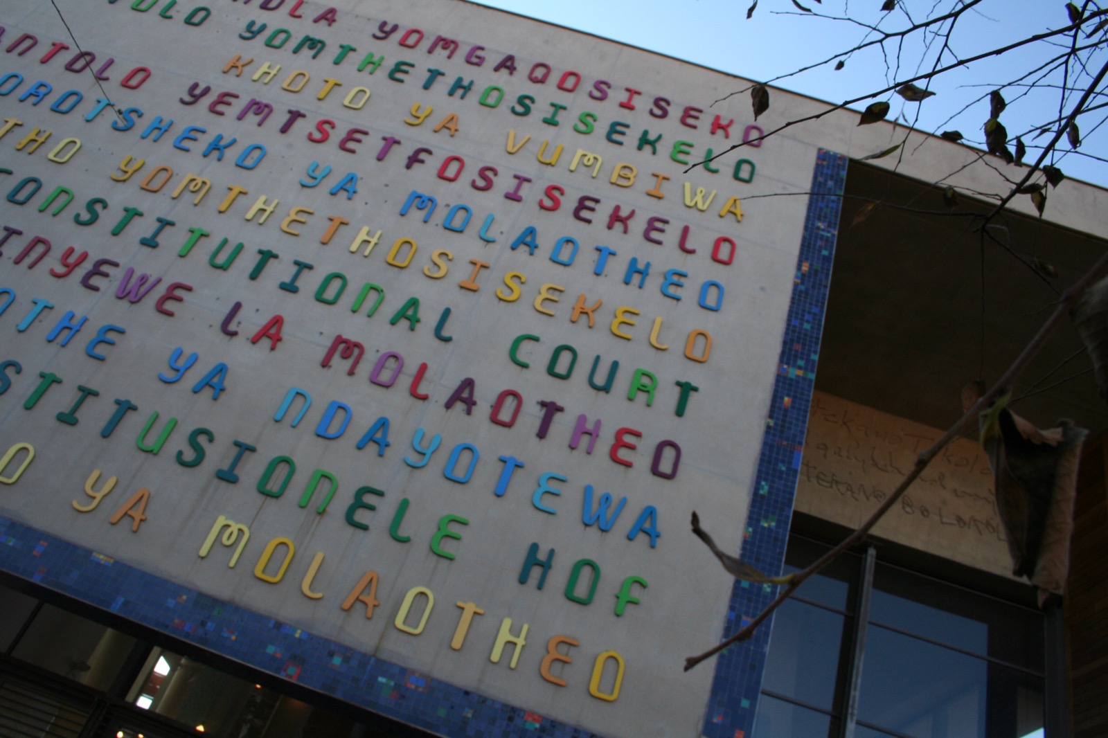 The entrance to the Constitutional Court of South Africa in Johannesburg, a modern building with tall, brightly coloured columns and the words 'Constitutional Court' rendered in several languages on a slanted canopy.