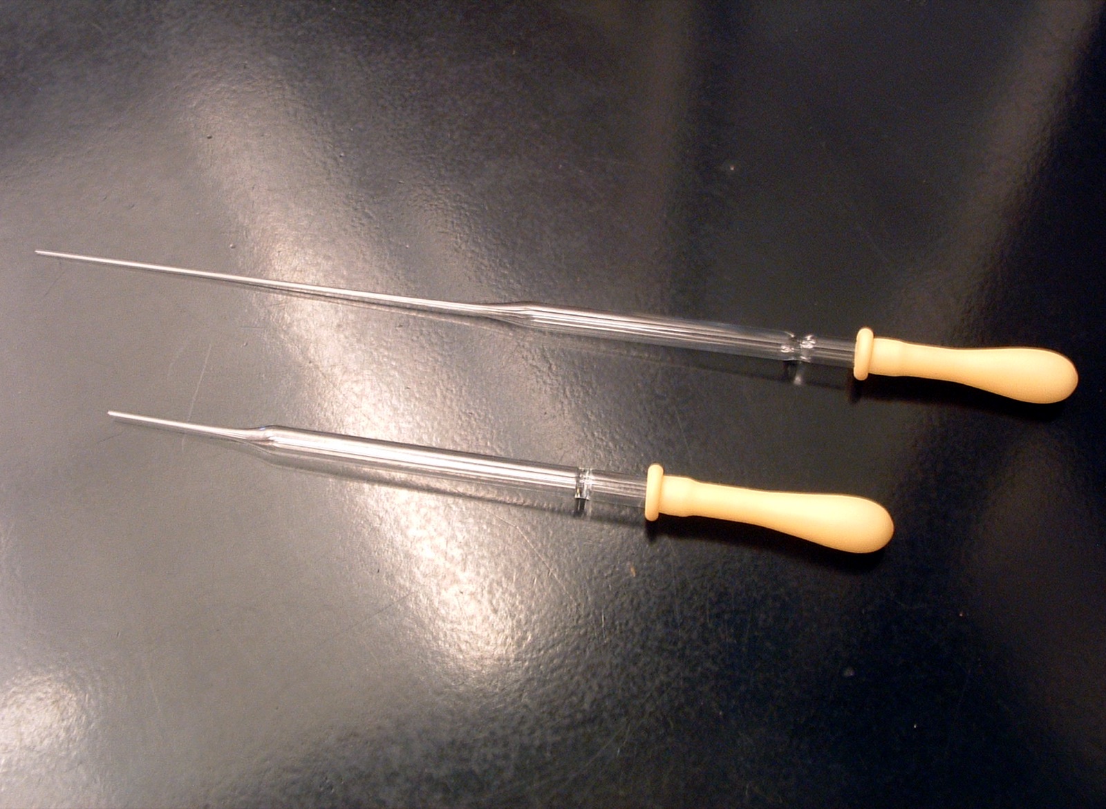 A close view of laboratory glass Pasteur pipettes and small vials arranged on a surface, slender glass tubes with tapered tips.