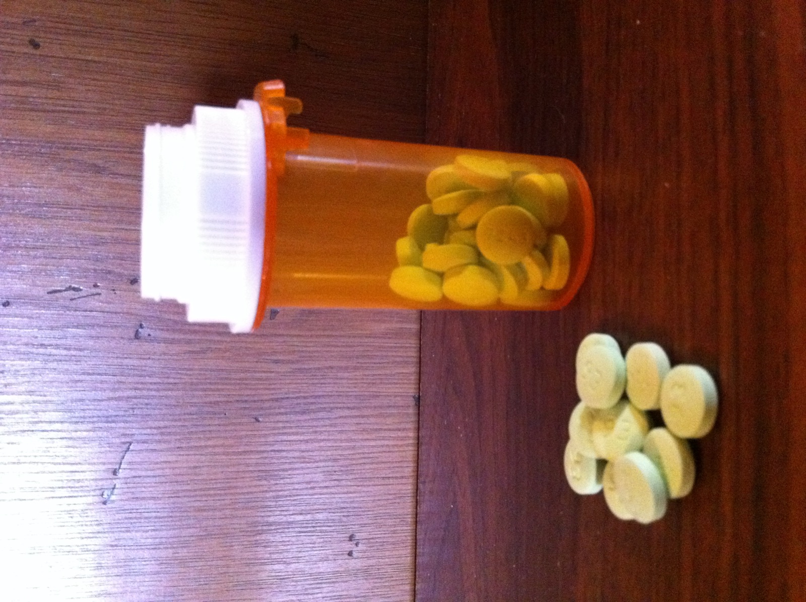 A bottle of benzodiazepine pills with several small tablets spilled in front of it on a plain surface.