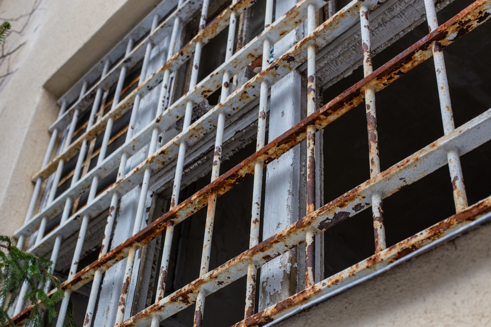 Close-up of rusted metal bars over weathered windows on the secure forensic-psychiatric pavilion at Säter hospital in Sweden, paint peeling, the glass dark behind the grille.