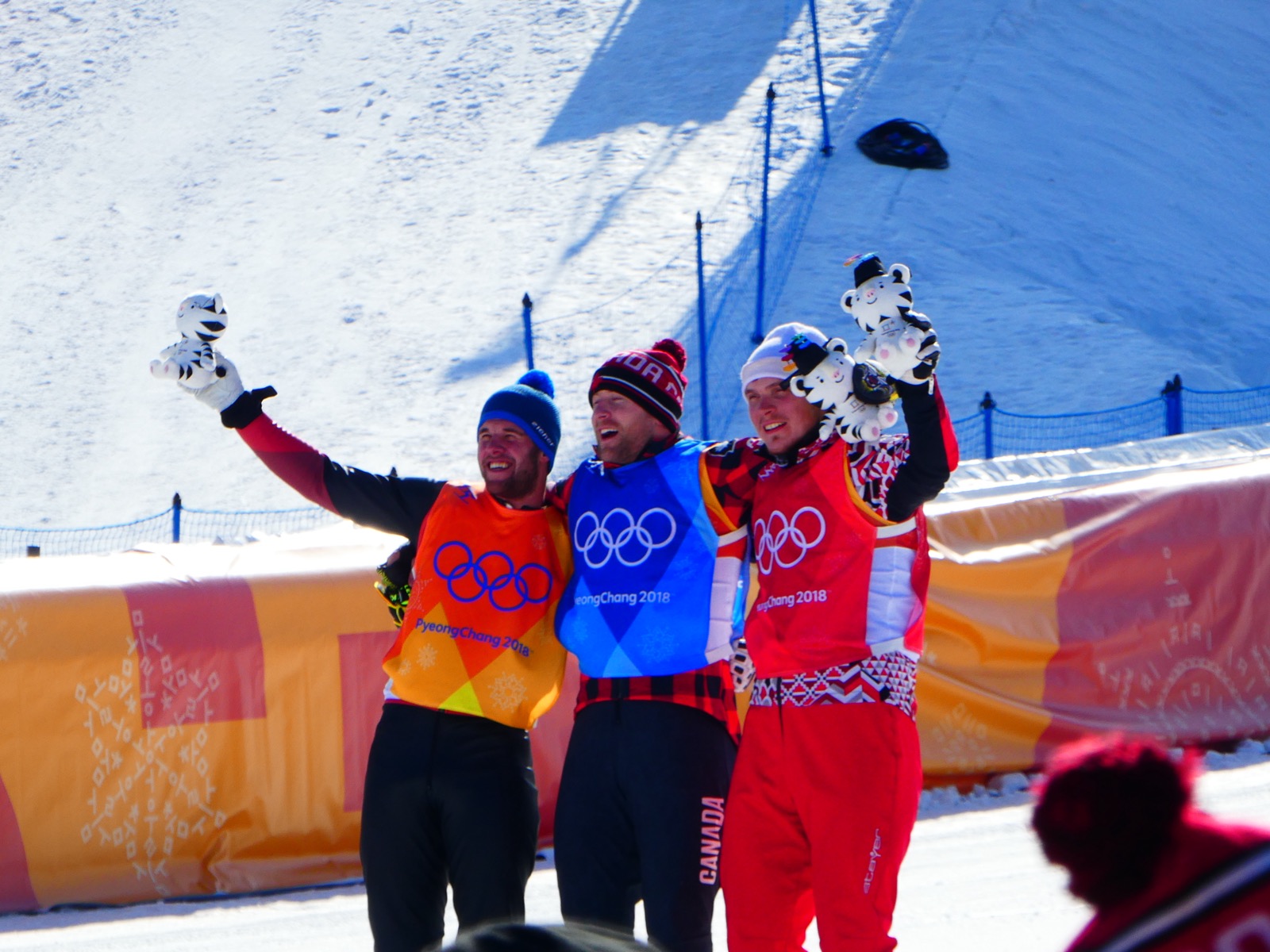 Athletes on a medal podium at the 2018 PyeongChang Winter Olympics, standing with medals and flowers in front of a crowd, a ski-cross event presentation.