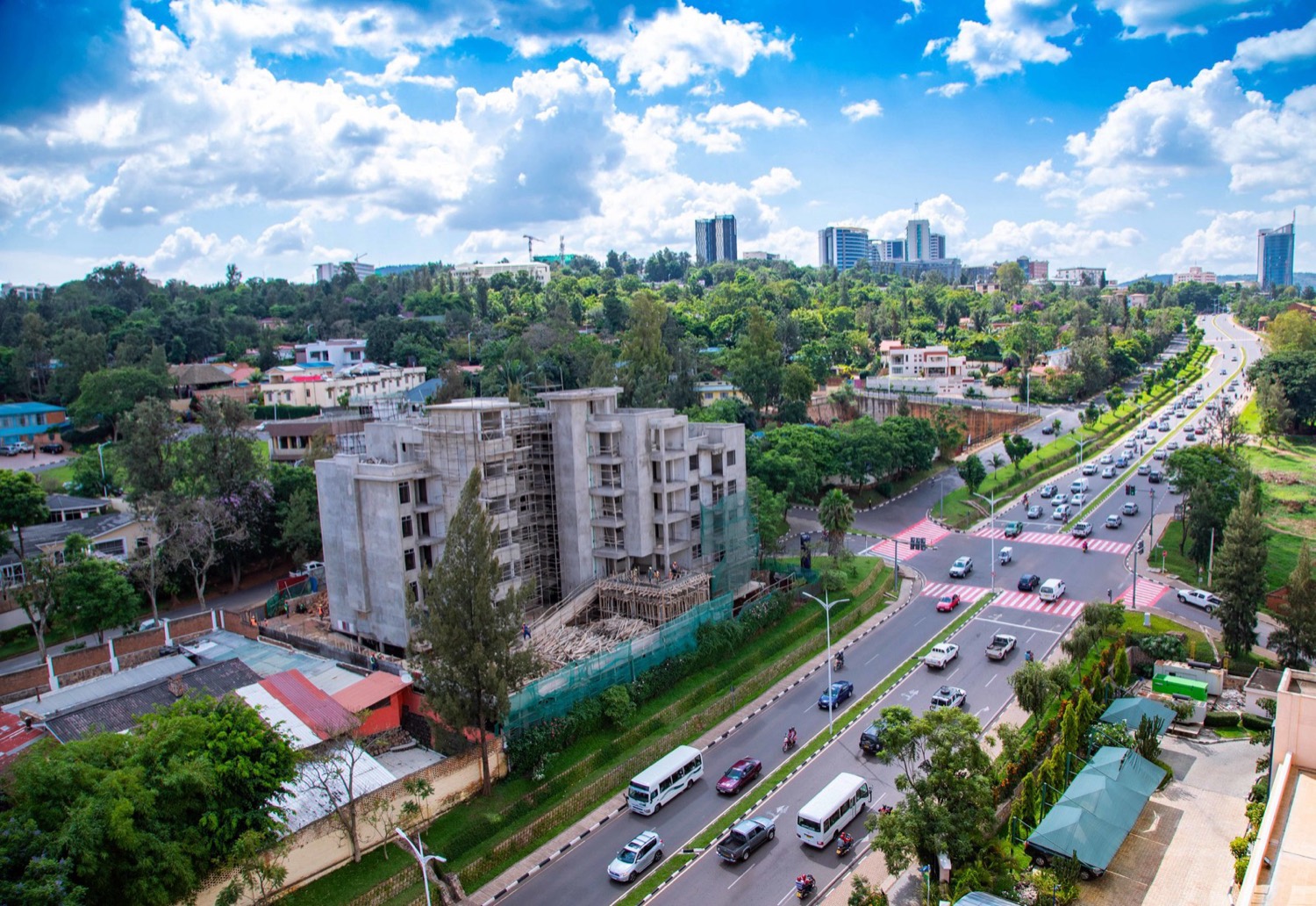 A high-angle view of a clean, modern street in Kigali, Rwanda, with paved roads, trees, and low buildings on green hillsides — a peaceful contemporary cityscape.