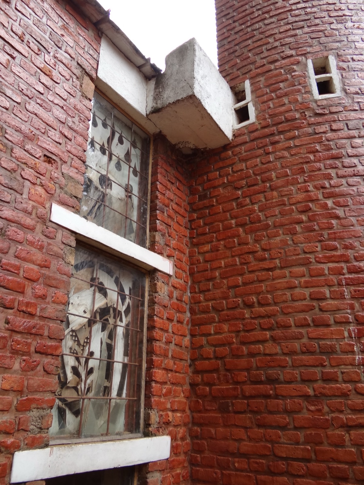 The brick exterior of the Catholic church at Nyamata, Rwanda, now a genocide memorial — red brick walls and a tower, with simple barred windows, under an overcast sky.
