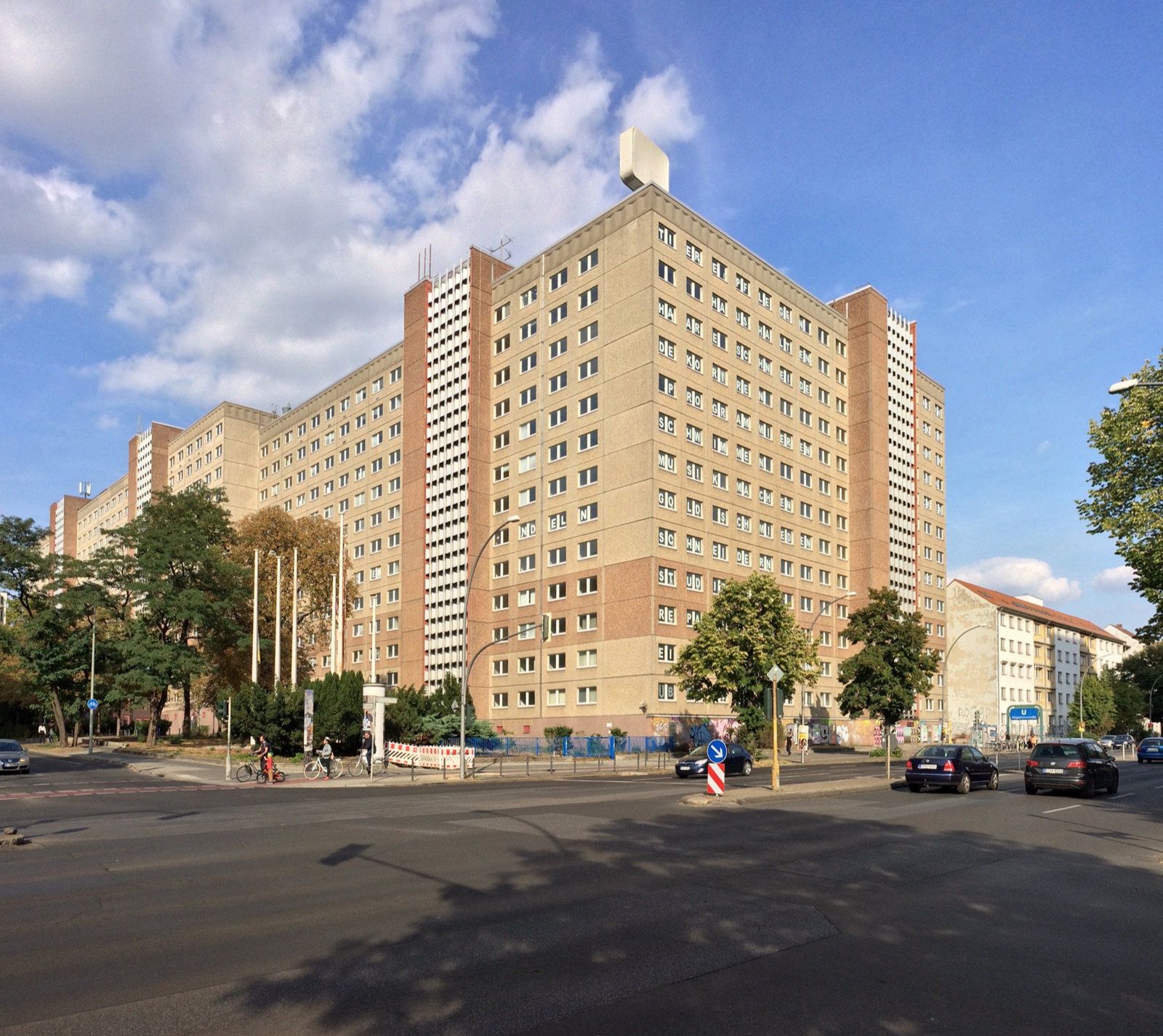 The former Stasi headquarters complex on the corner of Frankfurter Allee and Ruschestraße in Berlin-Lichtenberg — a 1960s GDR institutional building of brown-glazed concrete panels and grid windows, photographed from the street.