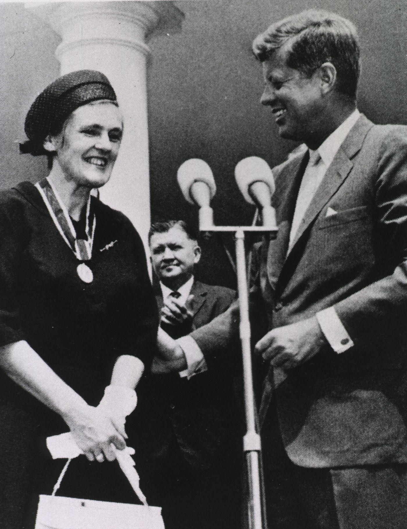 A 1962 black-and-white photograph of President John F. Kennedy presenting an award medal to Frances Oldham Kelsey, a woman in a dark dress and hat, both smiling, at an outdoor ceremony.