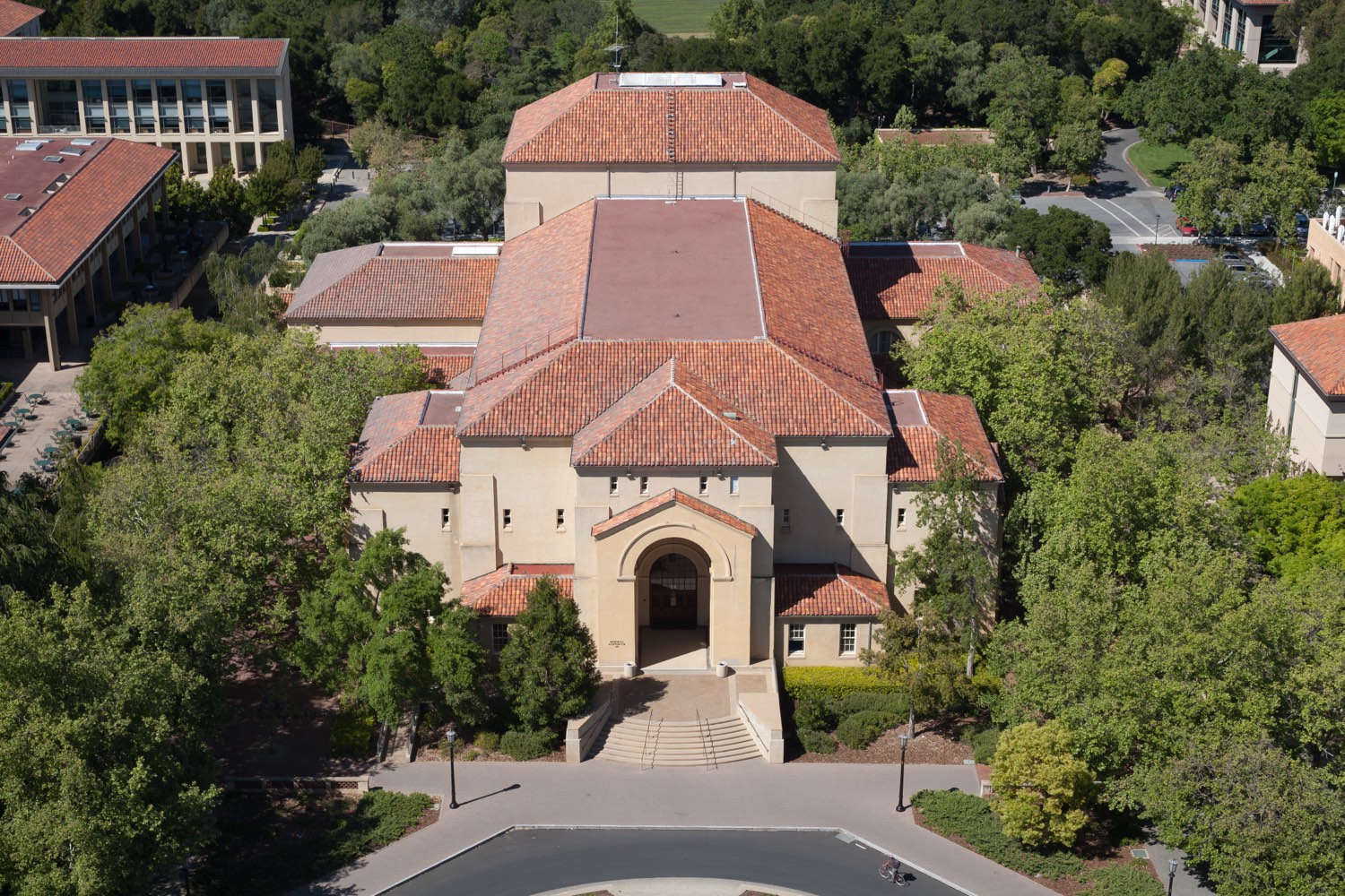 The campus of Stanford University in California, seen from above, with its sandstone buildings, red-tiled roofs, and palm-lined avenues among green hills.