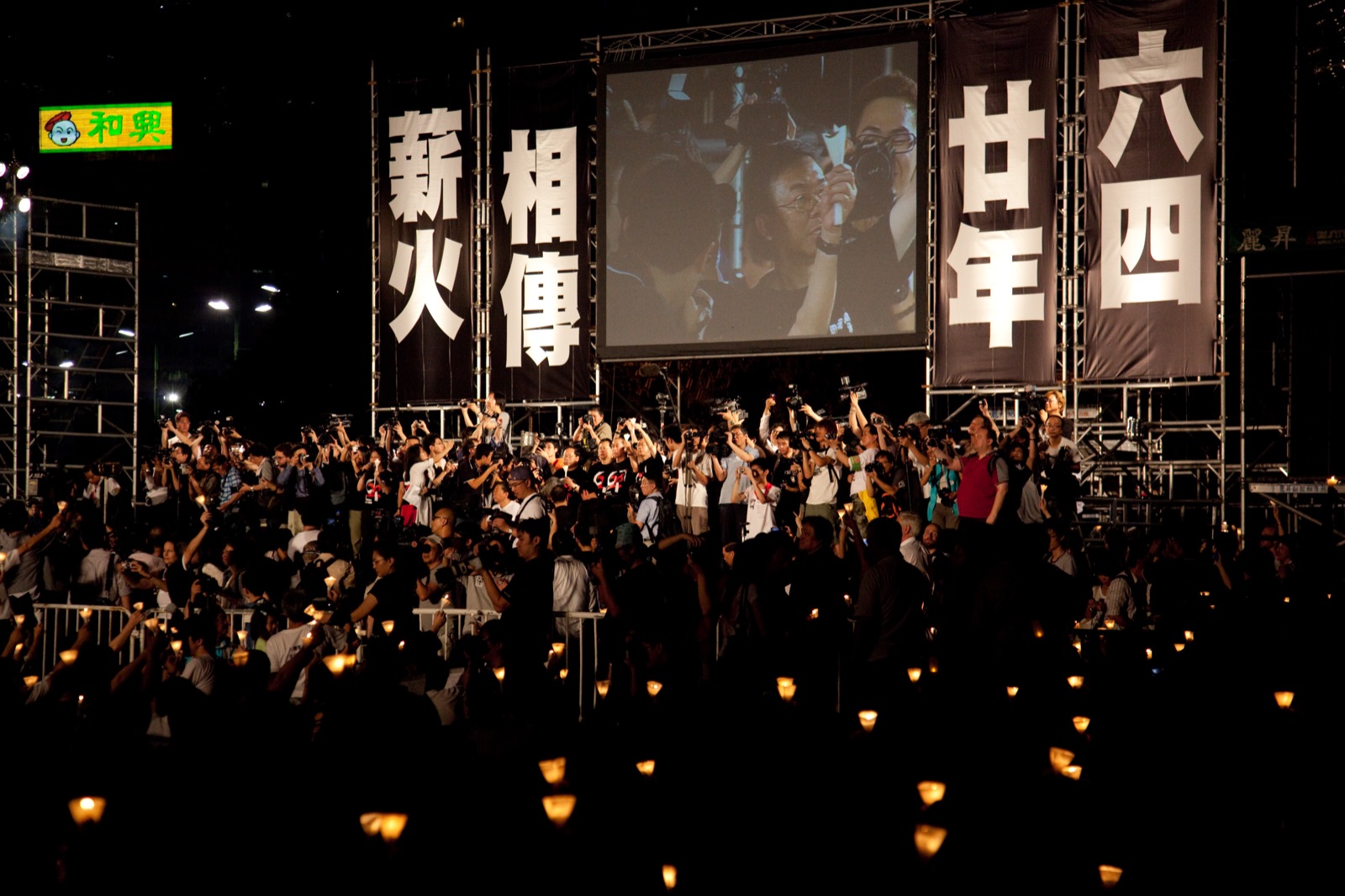 A nighttime candlelight vigil at Victoria Park in Hong Kong on June 4 — thousands of people seated in rows holding candles, with stage lighting visible in the background.