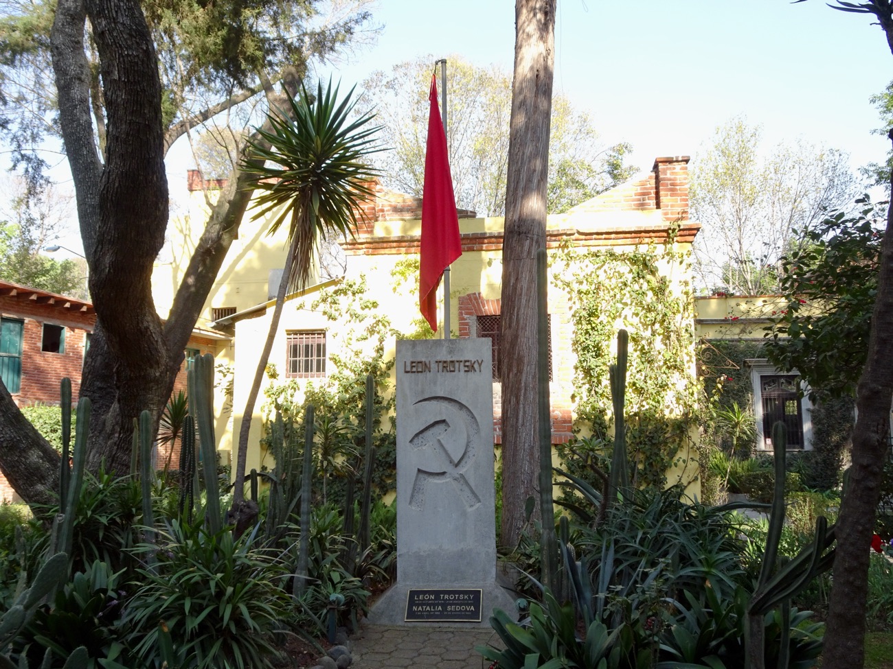 The grave and monument of Leon Trotsky and Natalia Sedova in the garden of the Coyoacán house, marked with a hammer and sickle and a red flag.