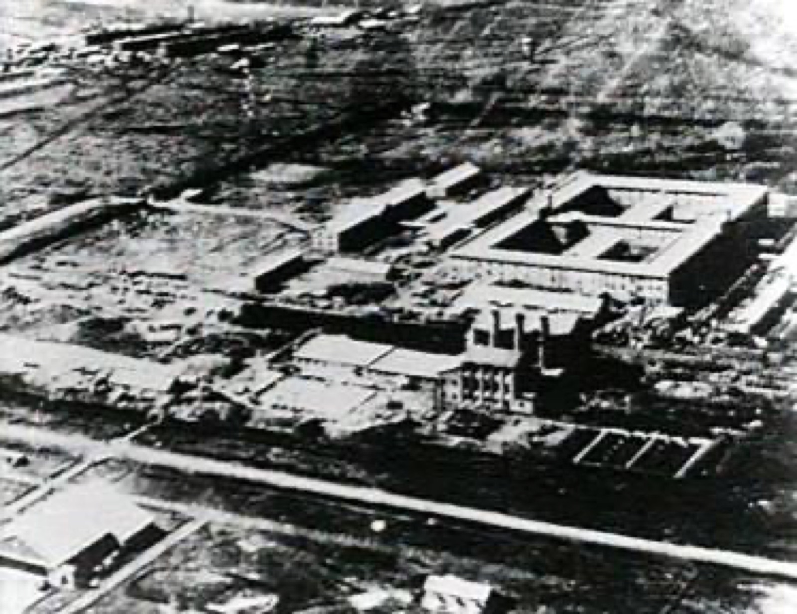 An aerial-style photograph of the Unit 731 main building complex taken in 1940 — a large multi-storey square-shaped institutional building with multiple wings, set in a flat agricultural landscape.