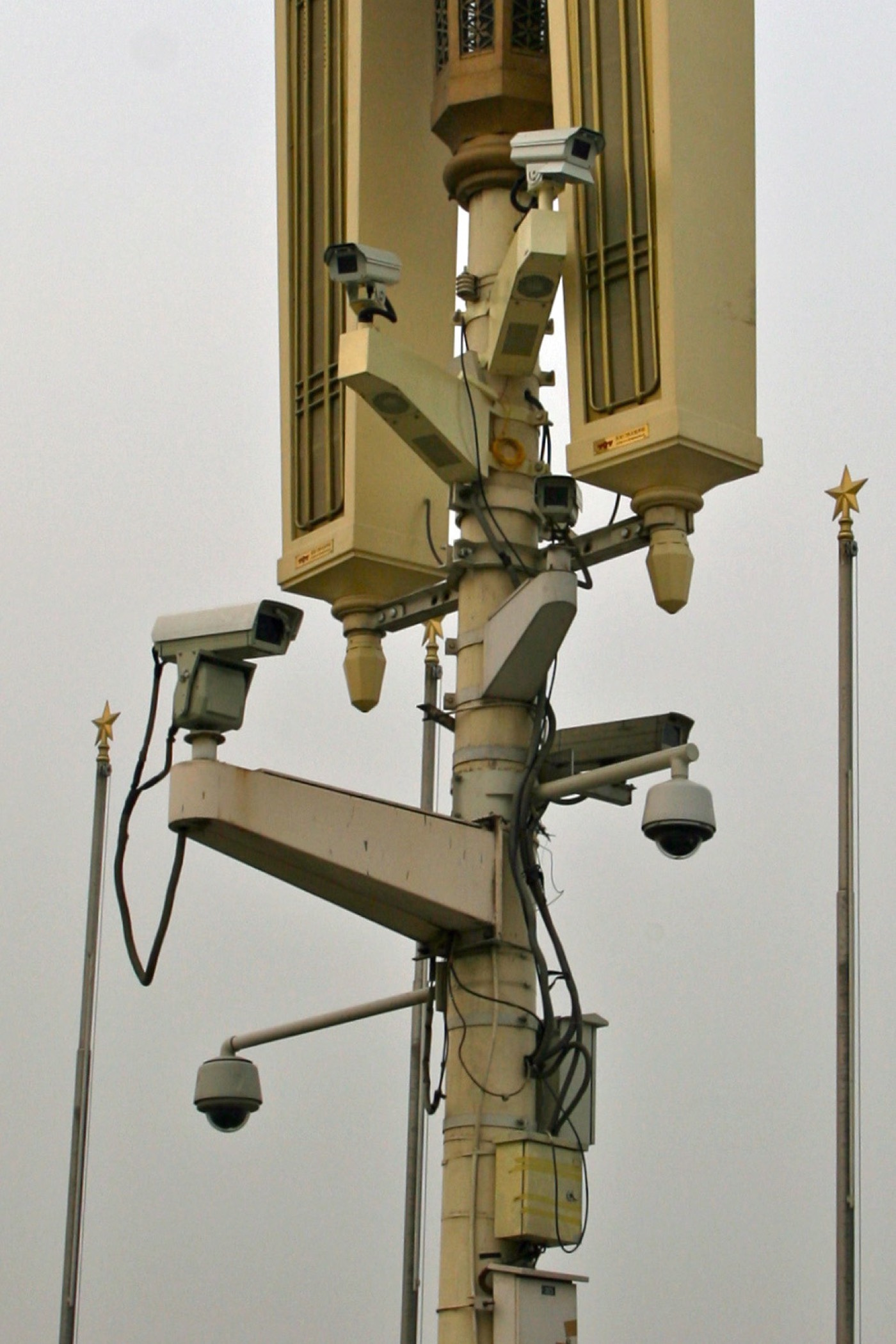 A cluster of surveillance cameras mounted on a pole against an overcast sky in China, several lenses pointing in different directions.