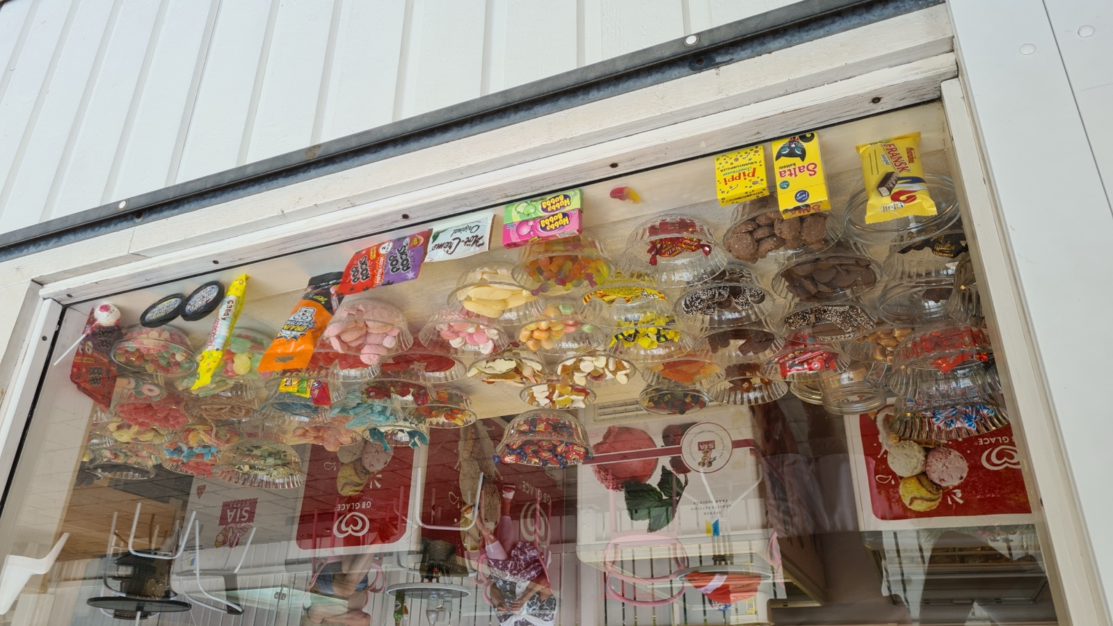 A Swedish pick-and-mix candy display seen through a shop window: rows of clear bowls filled with colourful loose sweets of many kinds.