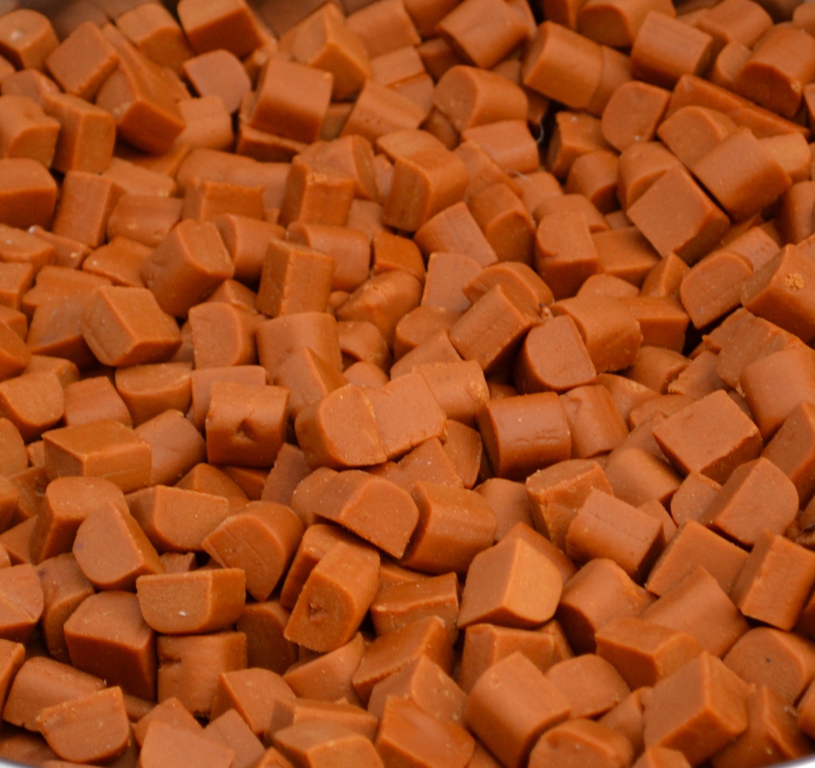 A close view of rows of wrapped and unwrapped toffees and caramels arranged on a surface, glossy brown sweets.